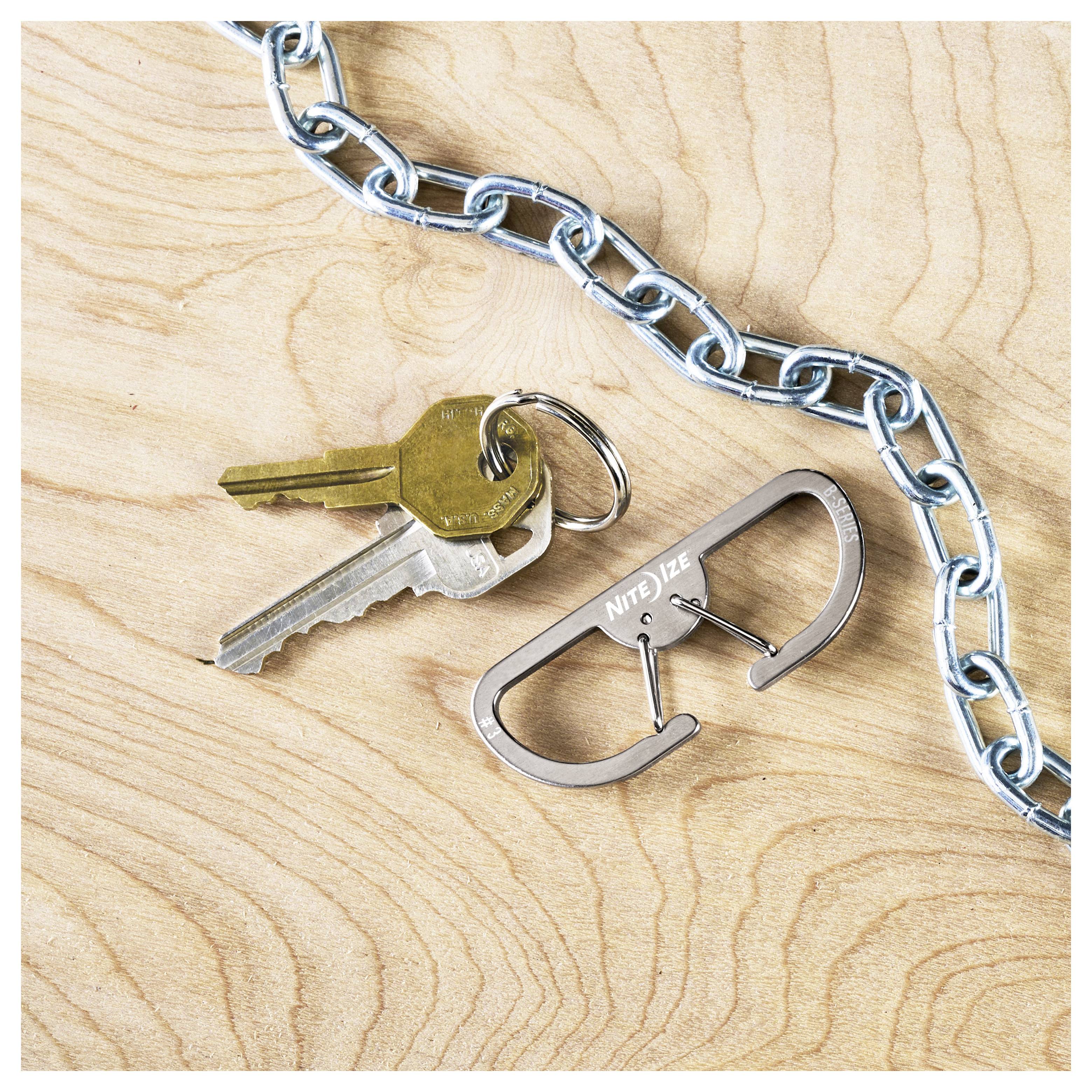 Ein Schlüsselbund, bestehend aus zwei Metallschlüsseln und einem Karabiner-Schlüsselanhänger, liegt auf einer Holzoberfläche neben einer Metallkette.