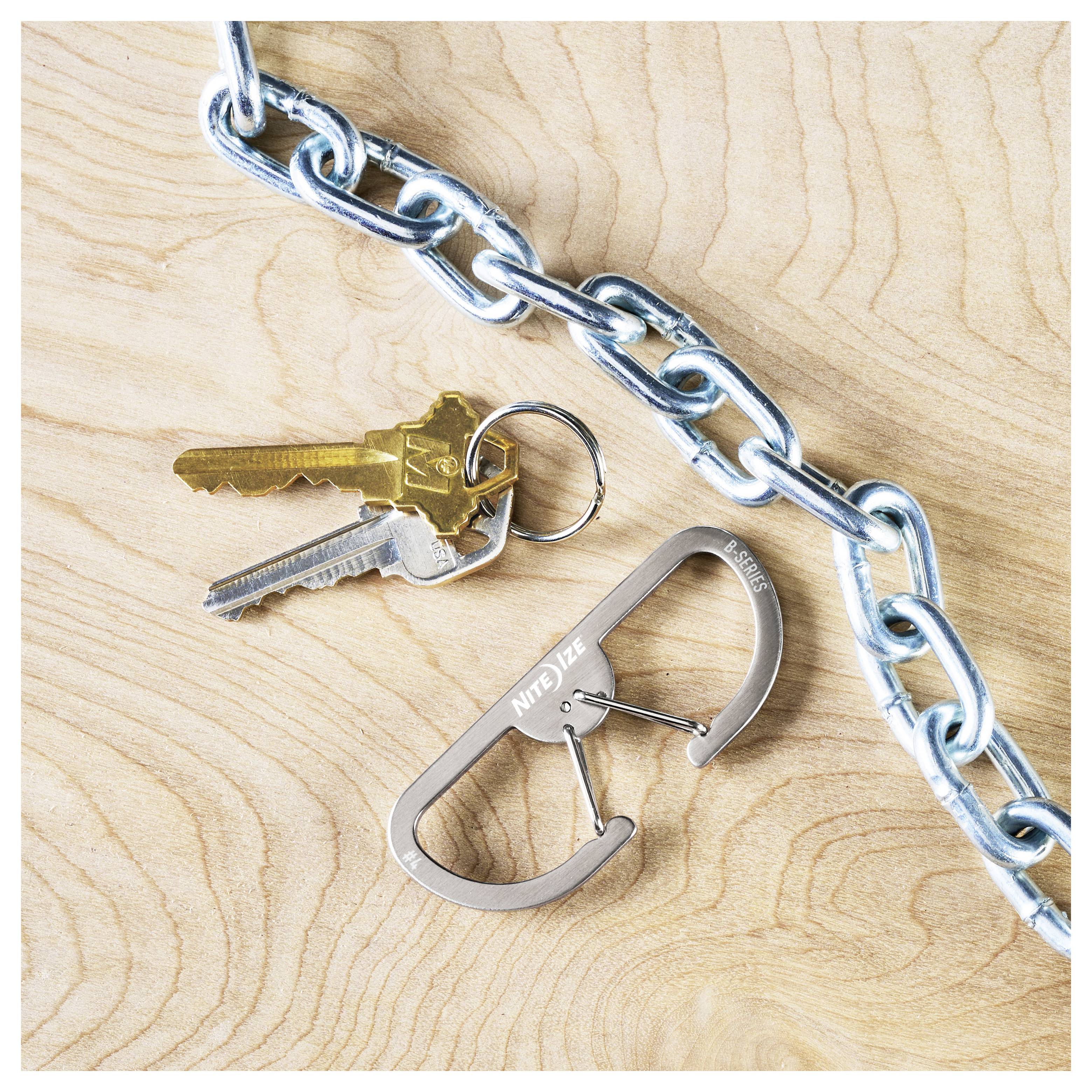 Ein Paar Schlüssel, die an einer Metallkette mit einem Karabiner auf einer Holzoberfläche befestigt sind. Der Karabiner ist mit dem Schriftzug 