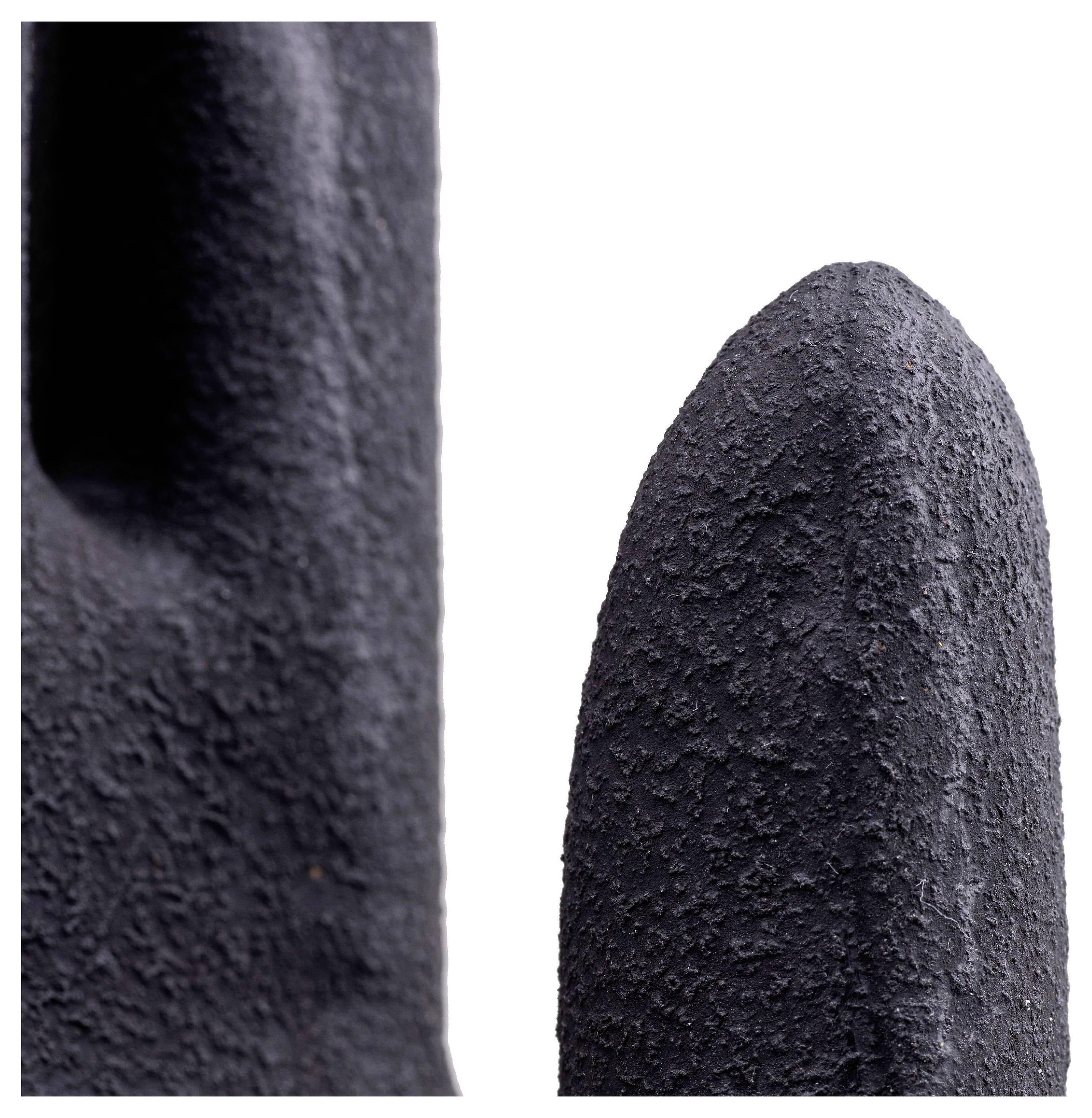 Eine Nahaufnahme von zwei texturierten, abstrakten schwarzen Skulpturen, die sich auf ihre raue Oberfläche und geschwungenen Formen vor einem weißen Hintergrund konzentriert.