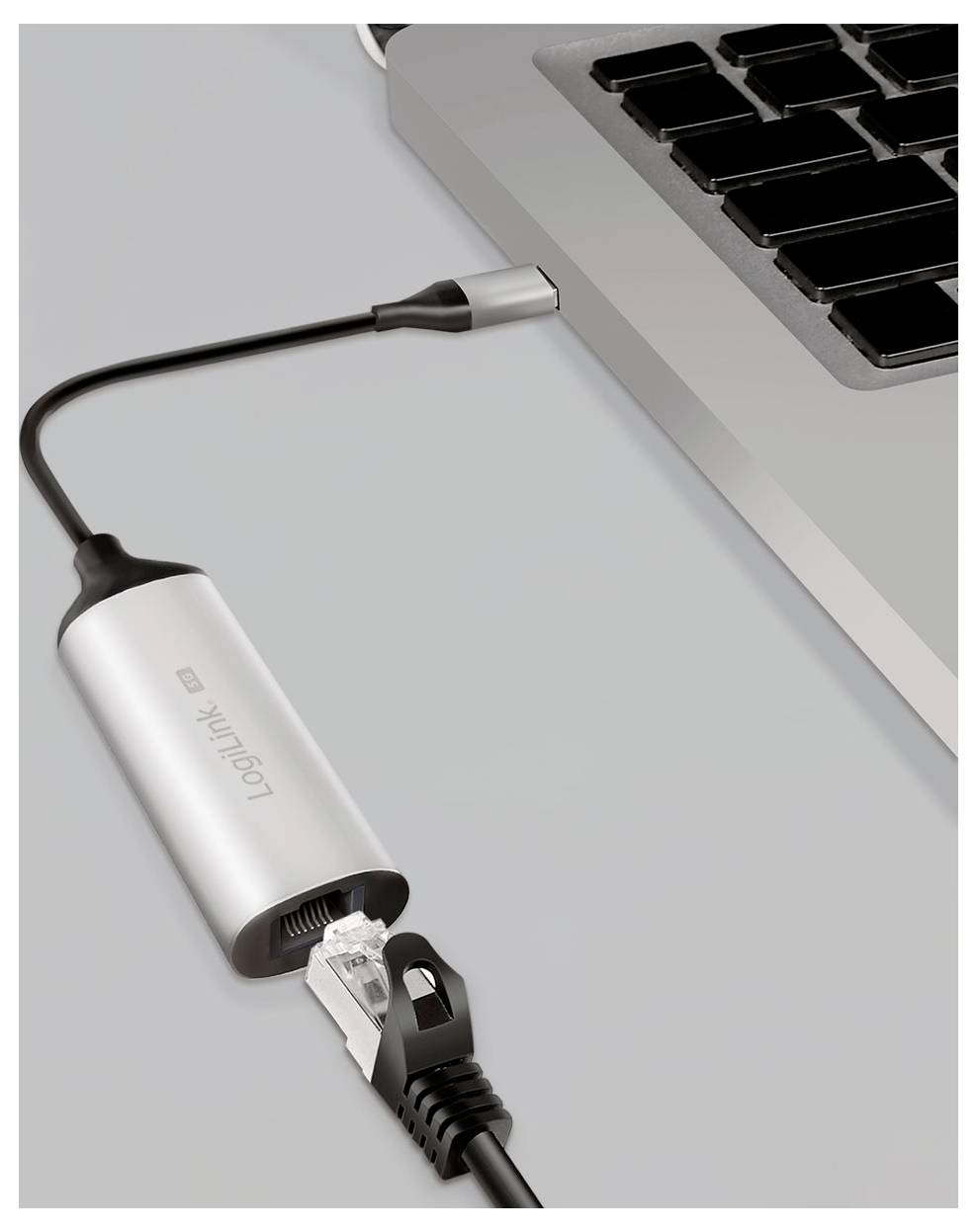 Ein silberner USB-C zu Ethernet-Adapter verbindet ein schwarzes Netzwerkkabel mit einem Laptop und ermöglicht dem Computer den kabelgebundenen Internetzugang.