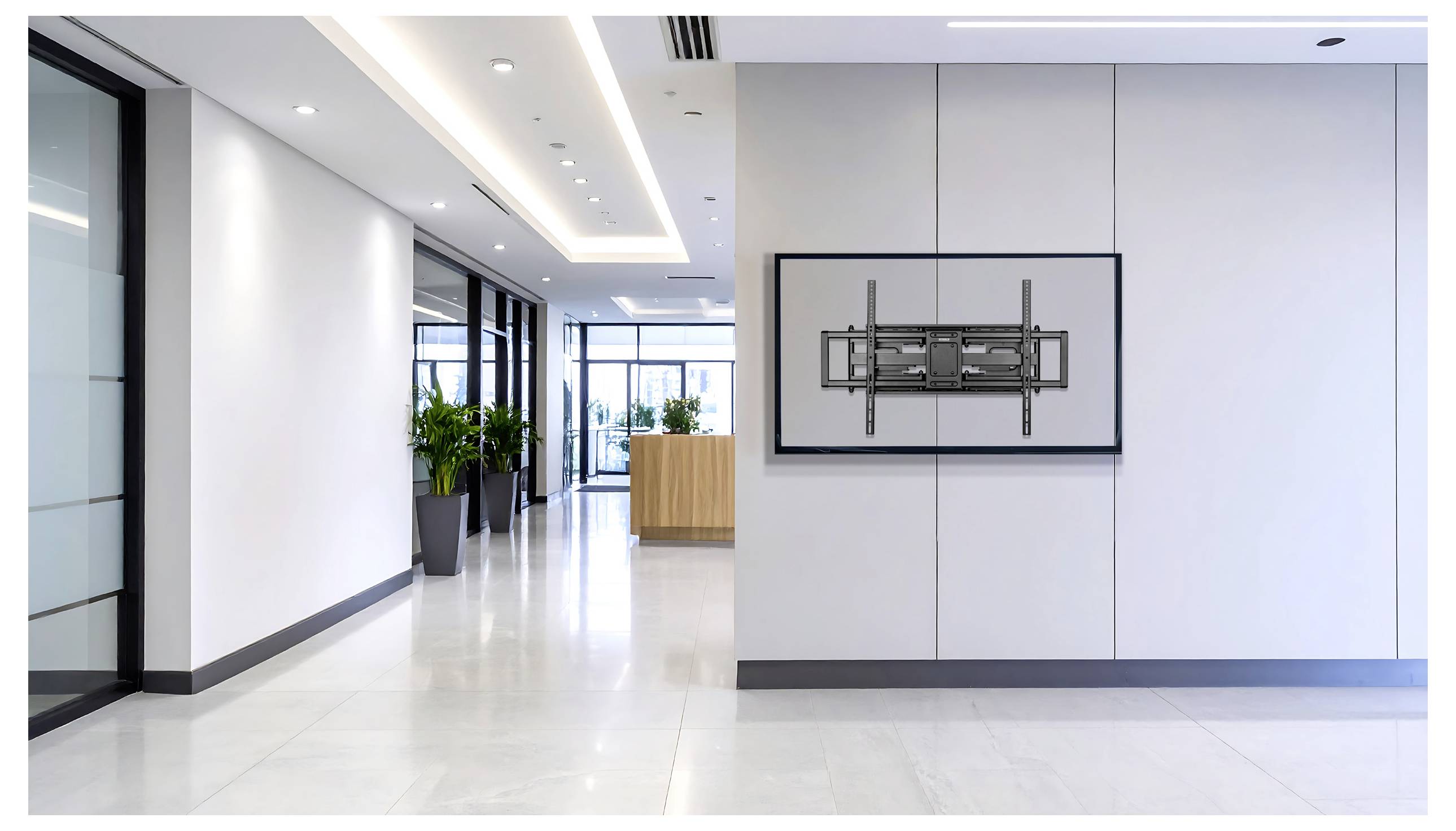 Ein moderner, heller Büroflur mit großen Fenstern, einem Empfangstresen im Hintergrund und einer an der Wand montierten TV-Halterung ohne Bildschirm.