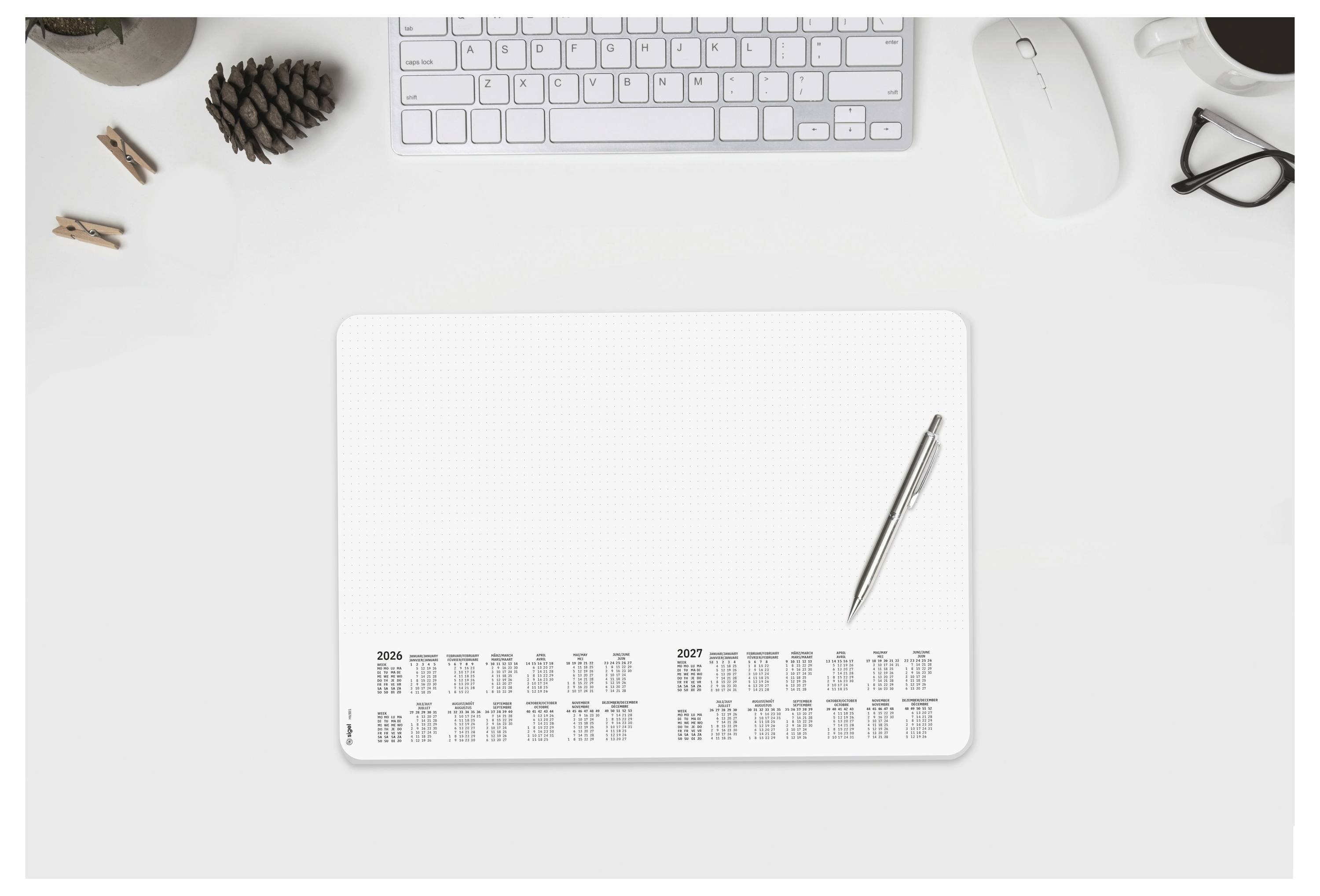 Draufsicht auf einen minimalistischen Schreibtisch mit leerem Notizbuch-Kalender, Stift, Tastatur, Maus, Brille und kleinen Tannenzapfen.