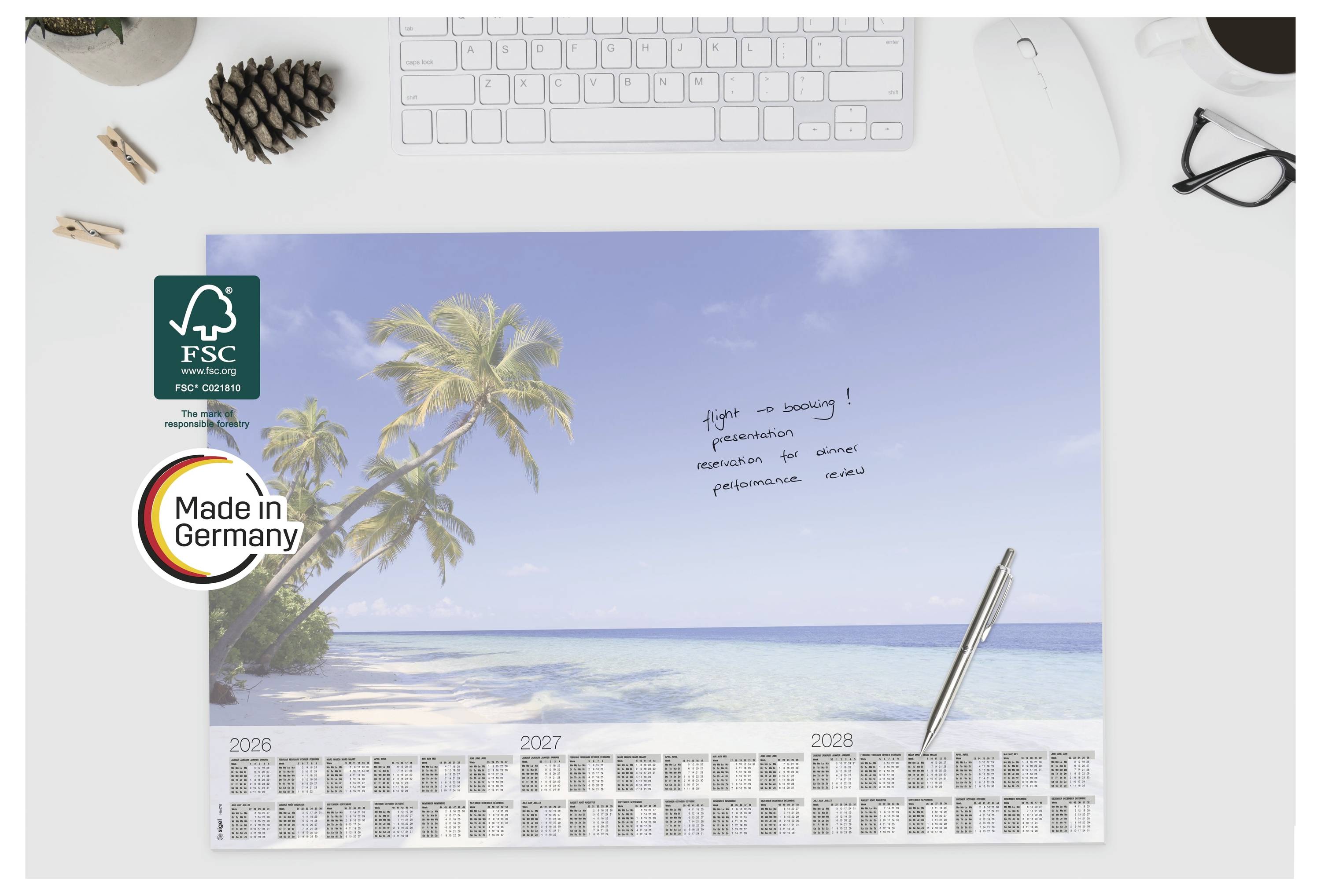Schreibtischkalender, der eine tropische Strandszene mit Palmen und einem kleinen handgeschriebenen Zettel zeigt; FSC- und „Made in Germany"-Logos befinden sich auf der linken Seite.