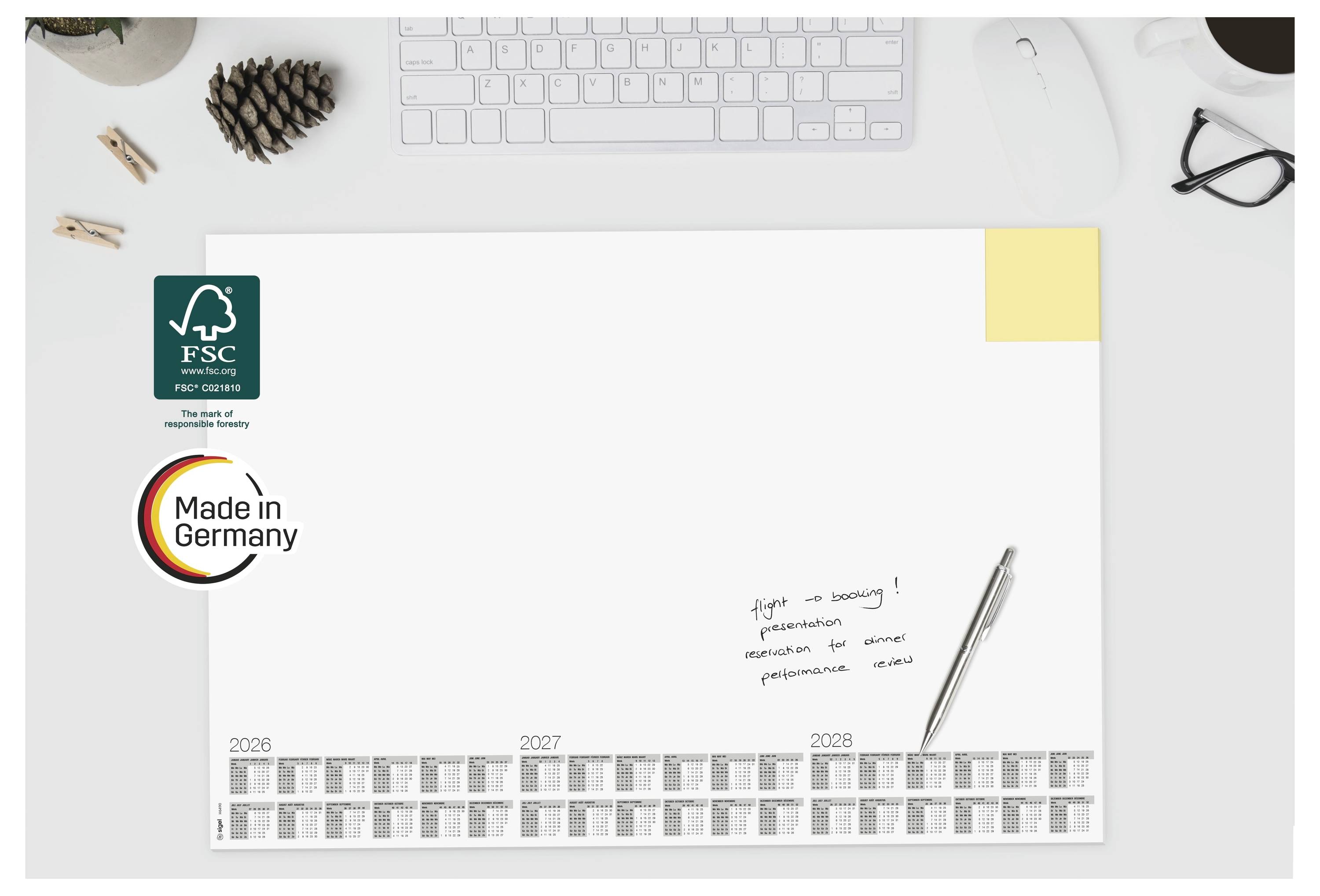 Schreibtischarbeitsplatz mit einem leeren FSC-zertifizierten Papierbogen, „Made in Germany"-Logo, Stift und Kalenderstreifen für 2026–2028 am unteren Rand.