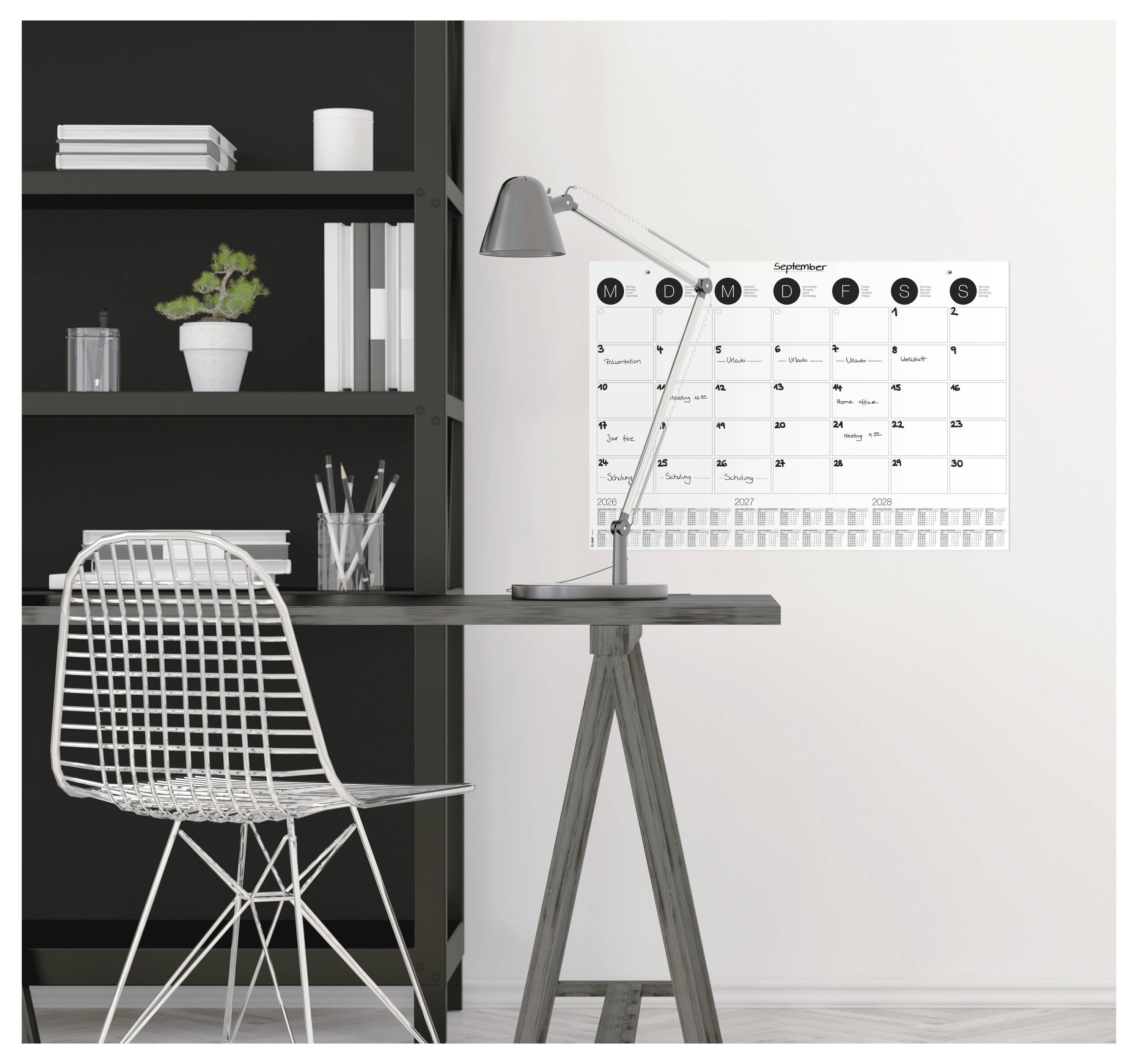 Arbeitsplatz mit einem Stuhl, Schreibtisch, Lampe und einem Wandkalender, der den Monat September zeigt. Regalsystem mit einer Pflanze und Büchern im Hintergrund.