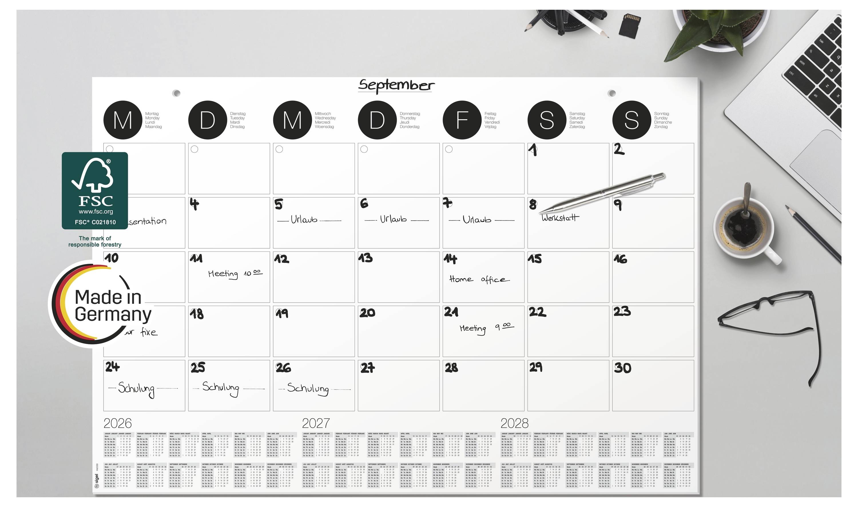 Septemberkalender an der Wand auf einem Schreibtisch, zeigt ein großteils leeres Monatsraster mit einigen handschriftlichen Notizen, einen Stift und ein "Made in Germany"-Logo.