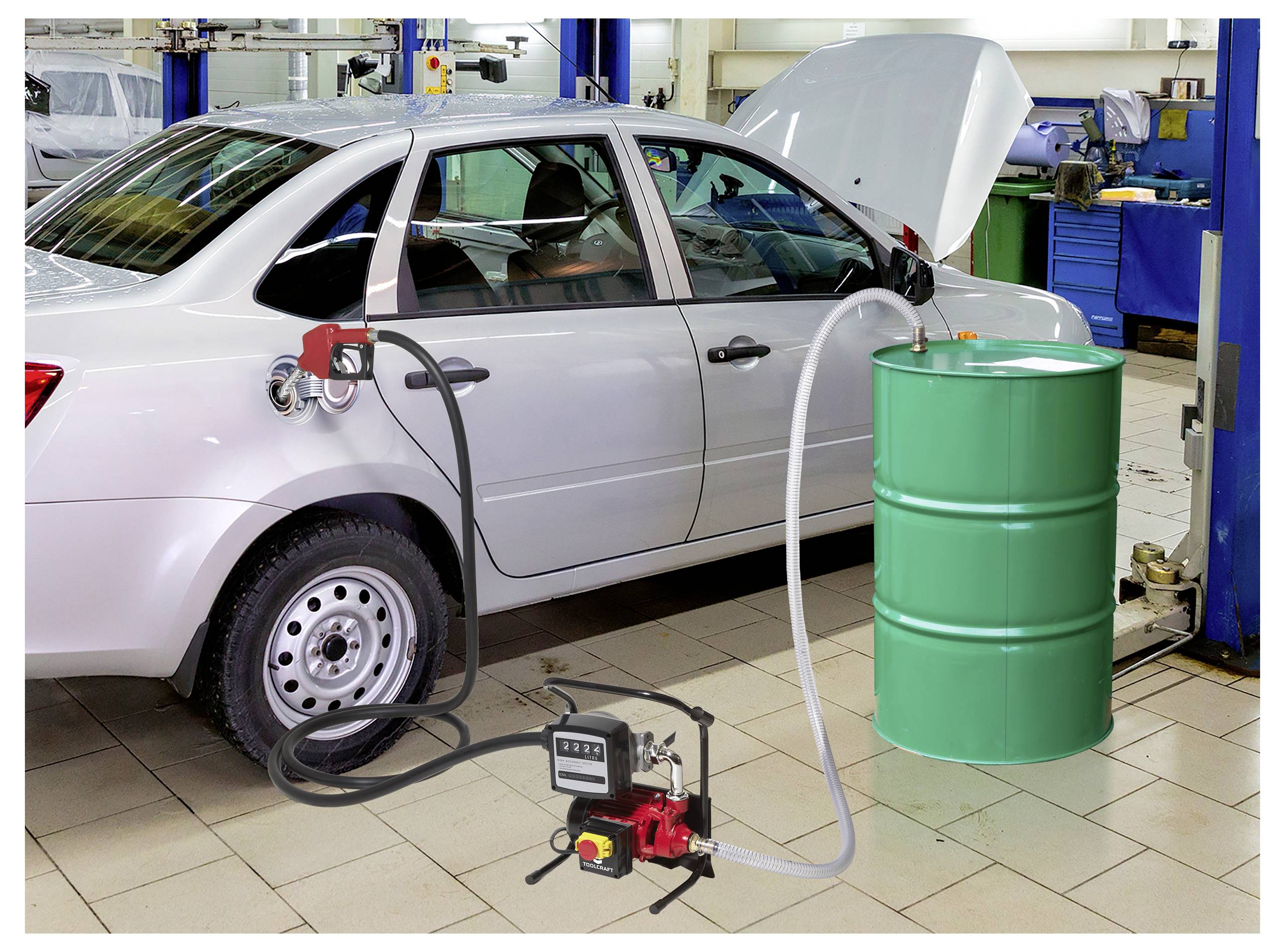 Ein Auto in einer Garage hat einen Schlauch, der von seinem Kraftstofftank zu einem grünen Fass verbunden ist. Die Motorhaube des Autos ist geöffnet, und im Hintergrund sind Werkzeuge zu sehen.