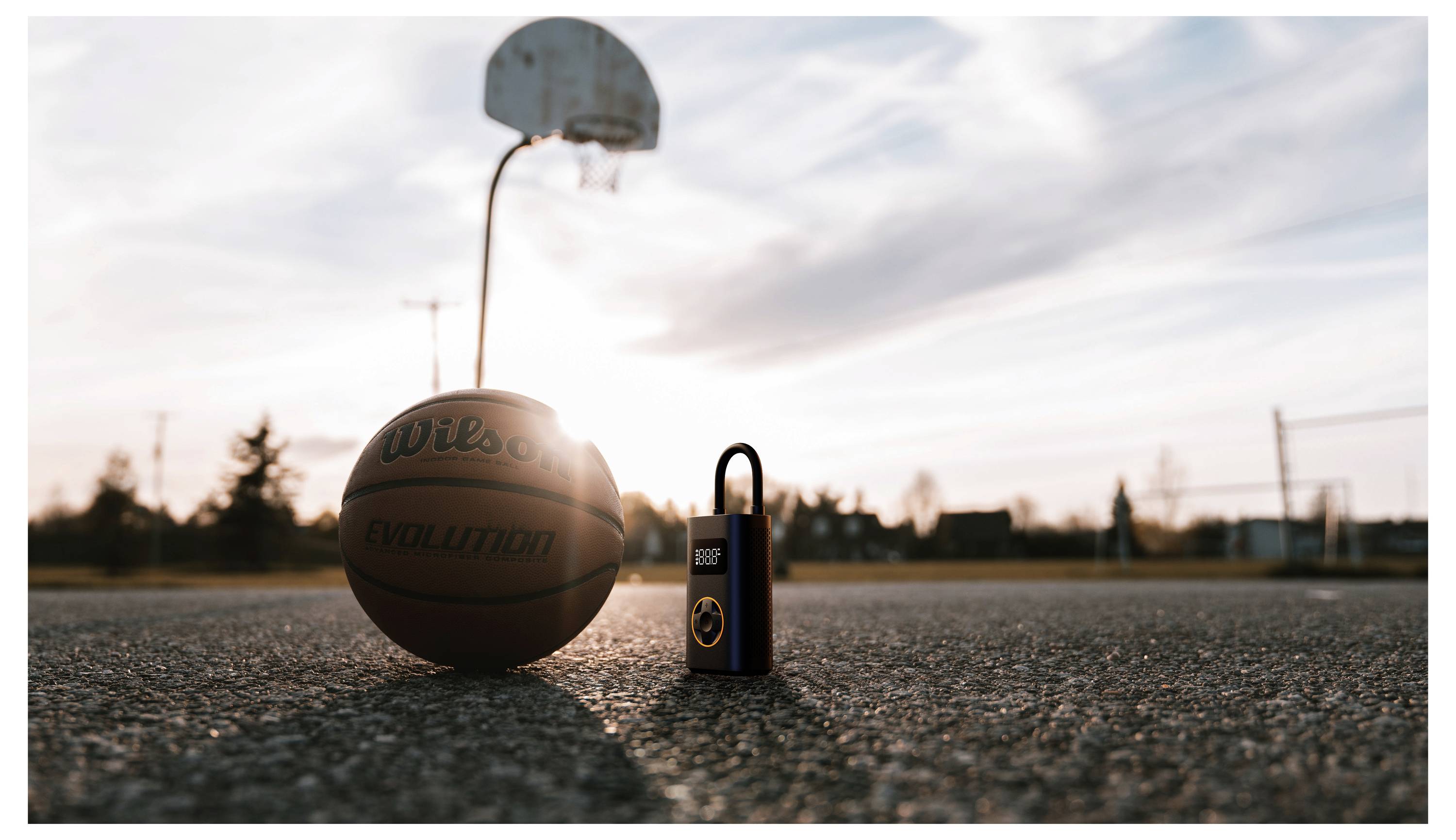 Ein Basketball und eine Flasche, die auf einem Outdoor-Basketballplatz bei Sonnenuntergang stehen, mit einem Basketballkorb im Hintergrund, wodurch eine ruhige Sportszene entsteht.