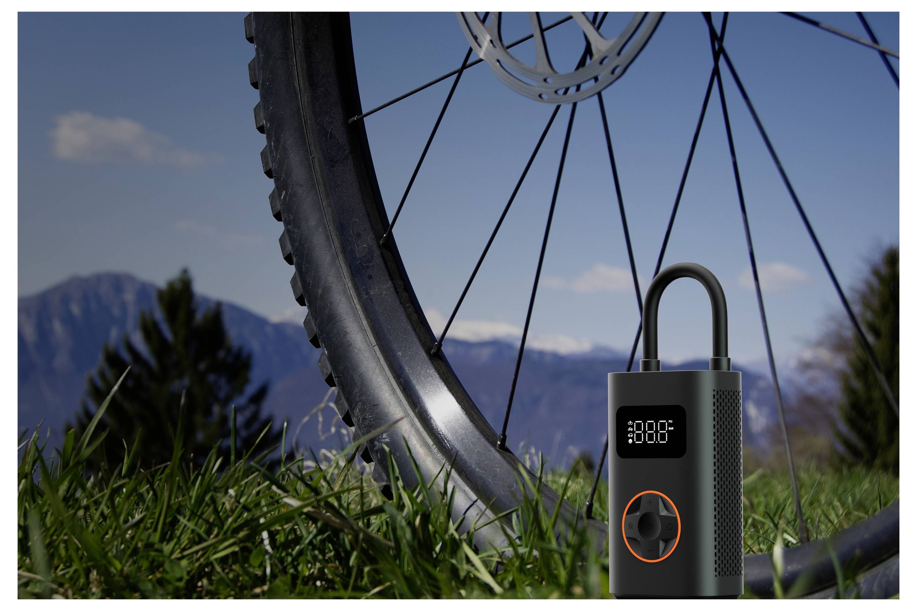 Eine tragbare Luftpumpe, die vor einem Fahrradrad im Freien platziert ist, mit bewölktem Himmel und Bergen im Hintergrund.