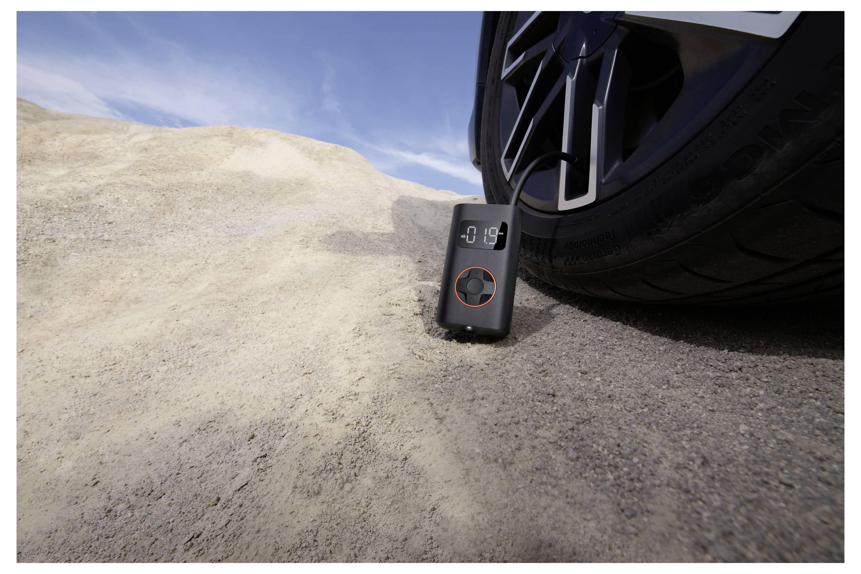 Ein digitales Reifendruckmessgerät, das an einem Reifen auf felsigem Gelände unter einem blauen Himmel angebracht ist.