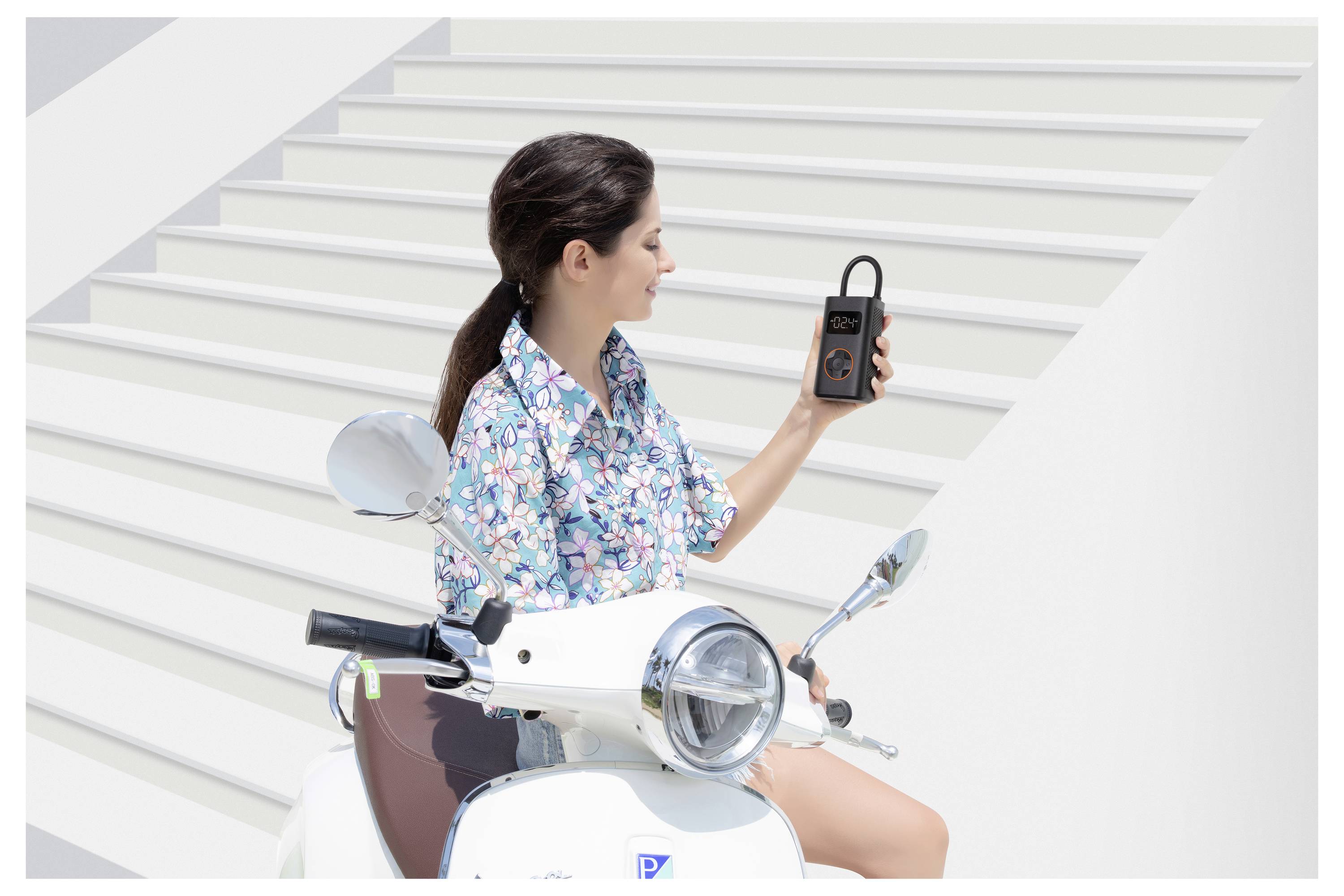 Eine Frau sitzt auf einem weißen Roller in der Nähe einer Treppe, hält ein elektronisches Gerät und betrachtet es aufmerksam.