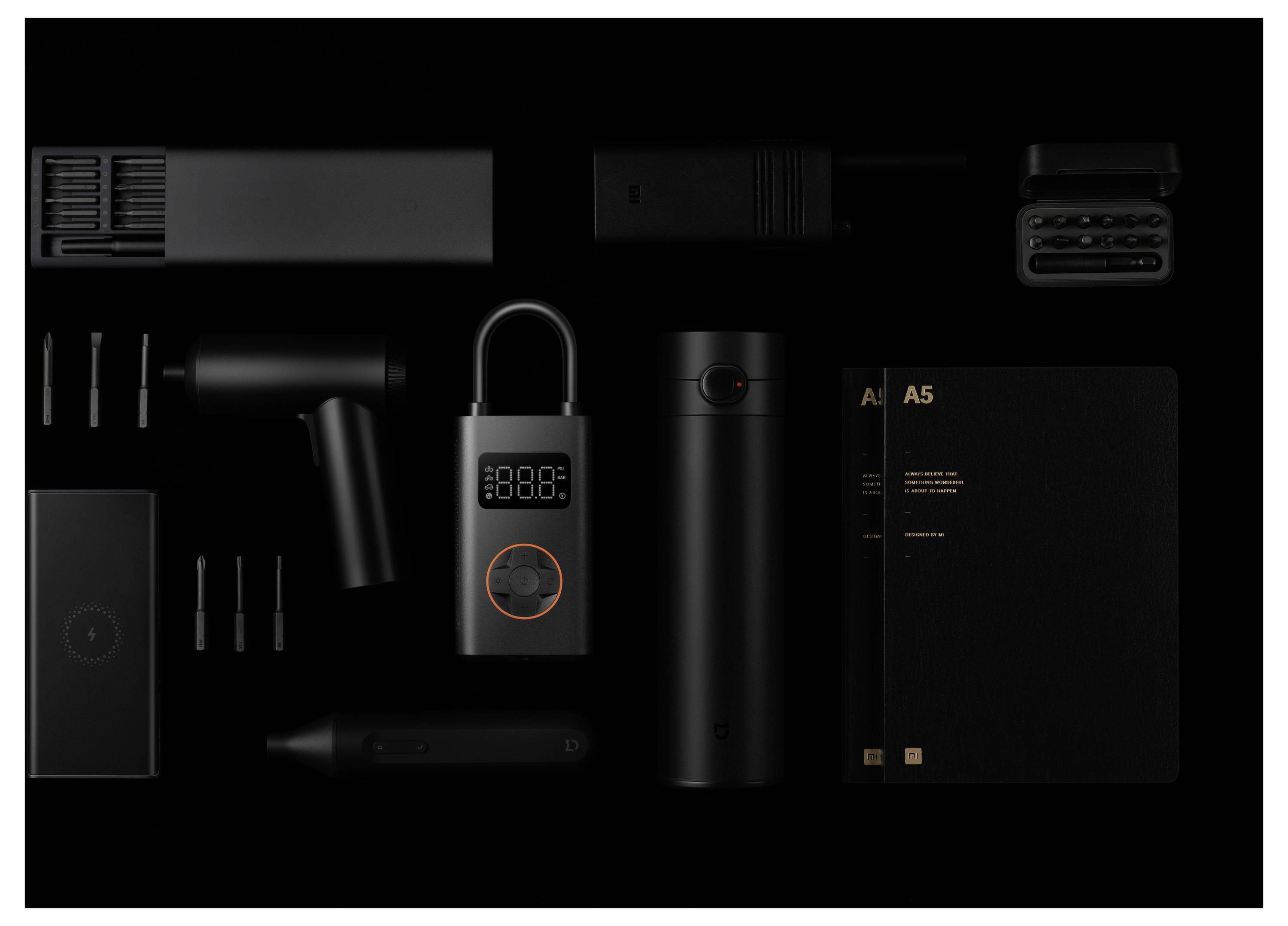 Sammlung schwarzer elektronischer Geräte und Werkzeuge vor einem dunklen Hintergrund, einschließlich eines mit A5 beschrifteten Notizbuchs, eines Smart-Locks und von Ladegeräten.