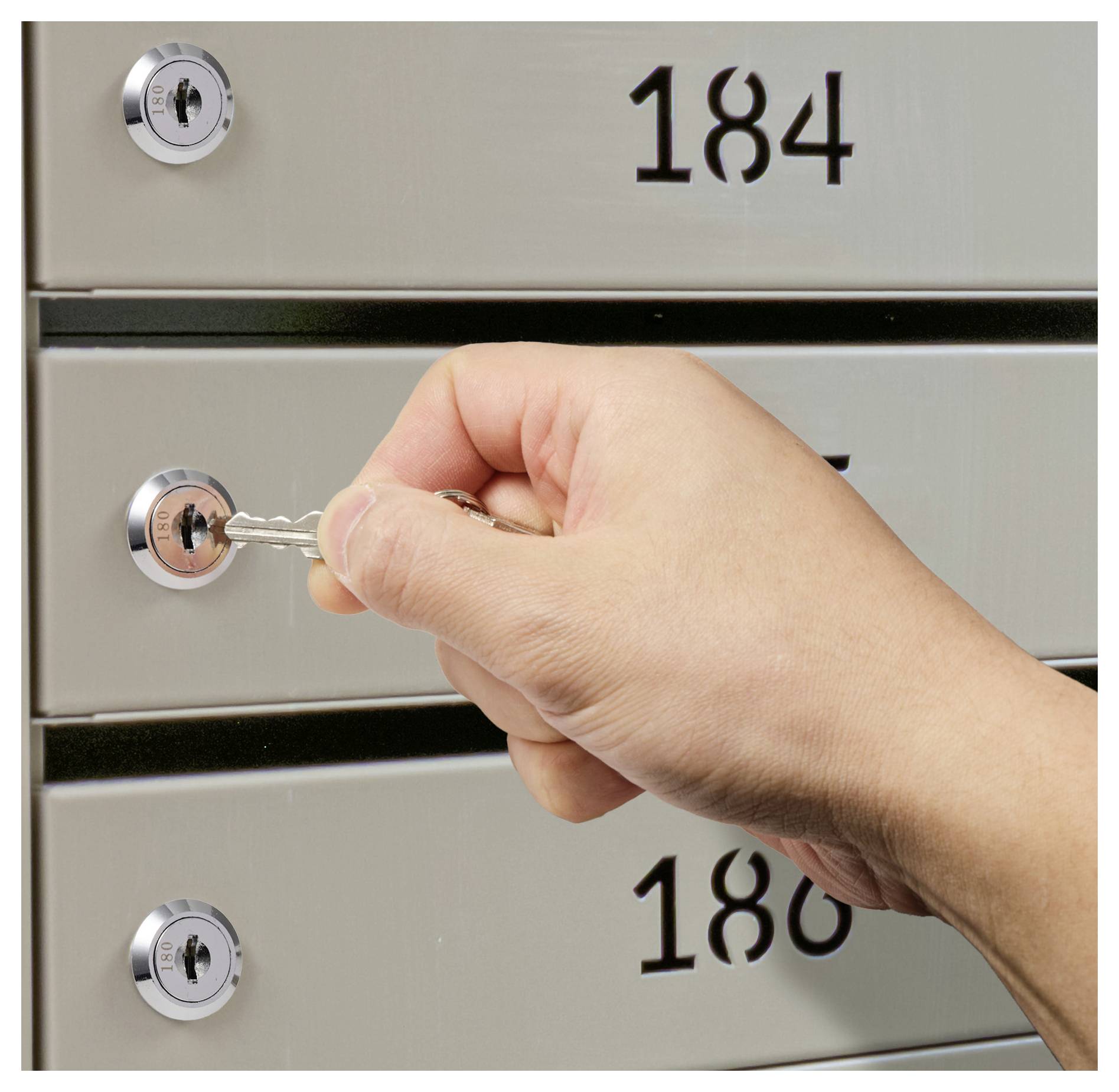 Eine Hand steckt einen Schlüssel in das Schloss des Briefkastens mit der Nummer 184, wobei die Briefkästen 185 und 186 darüber und darunter sichtbar sind.