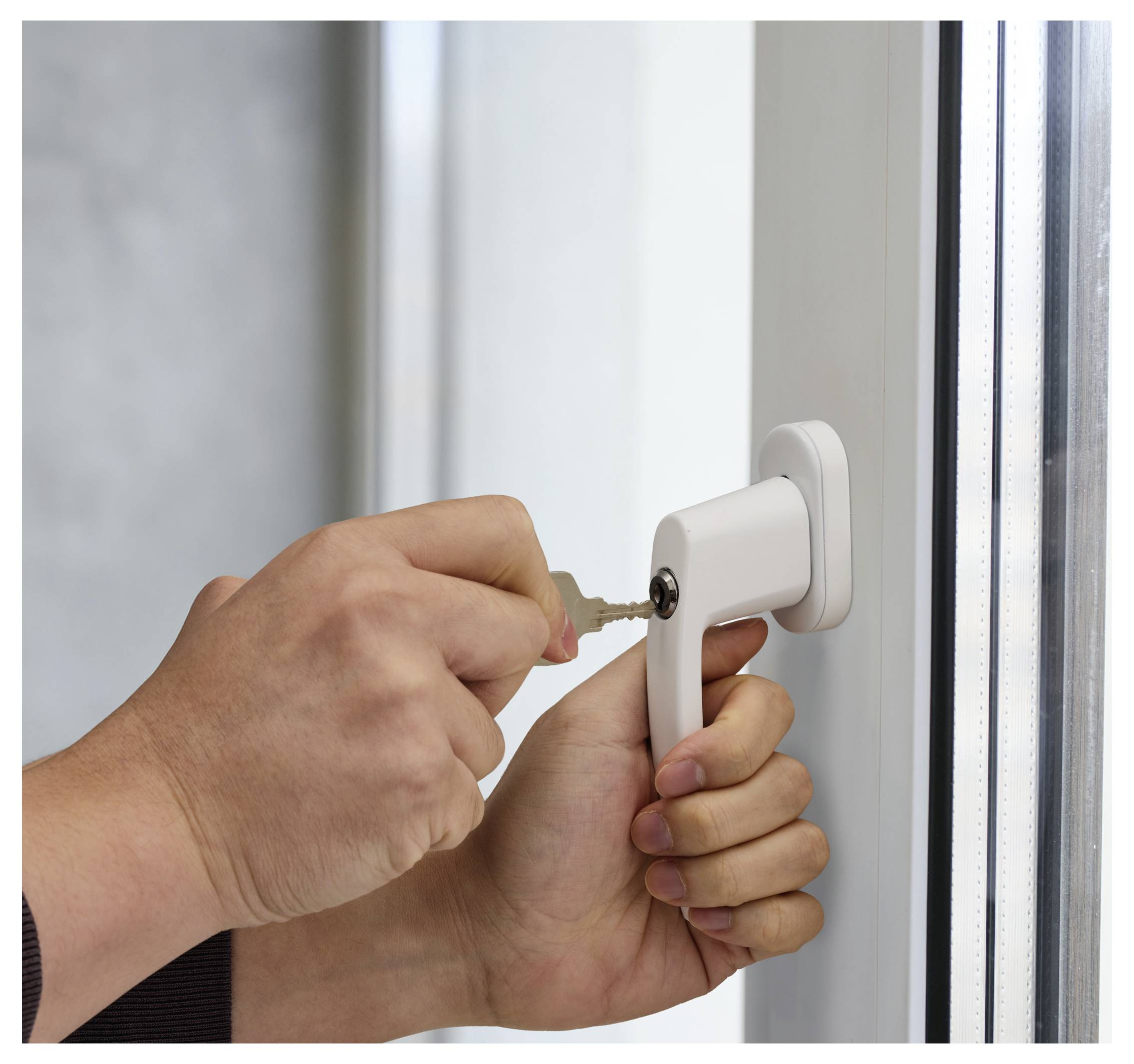 Eine Hand einer Person schiebt einen Schlüssel in das Schloss eines Fenstergriffs, was auf Fenstersicherheit oder eine Verriegelungsaktion hindeutet.