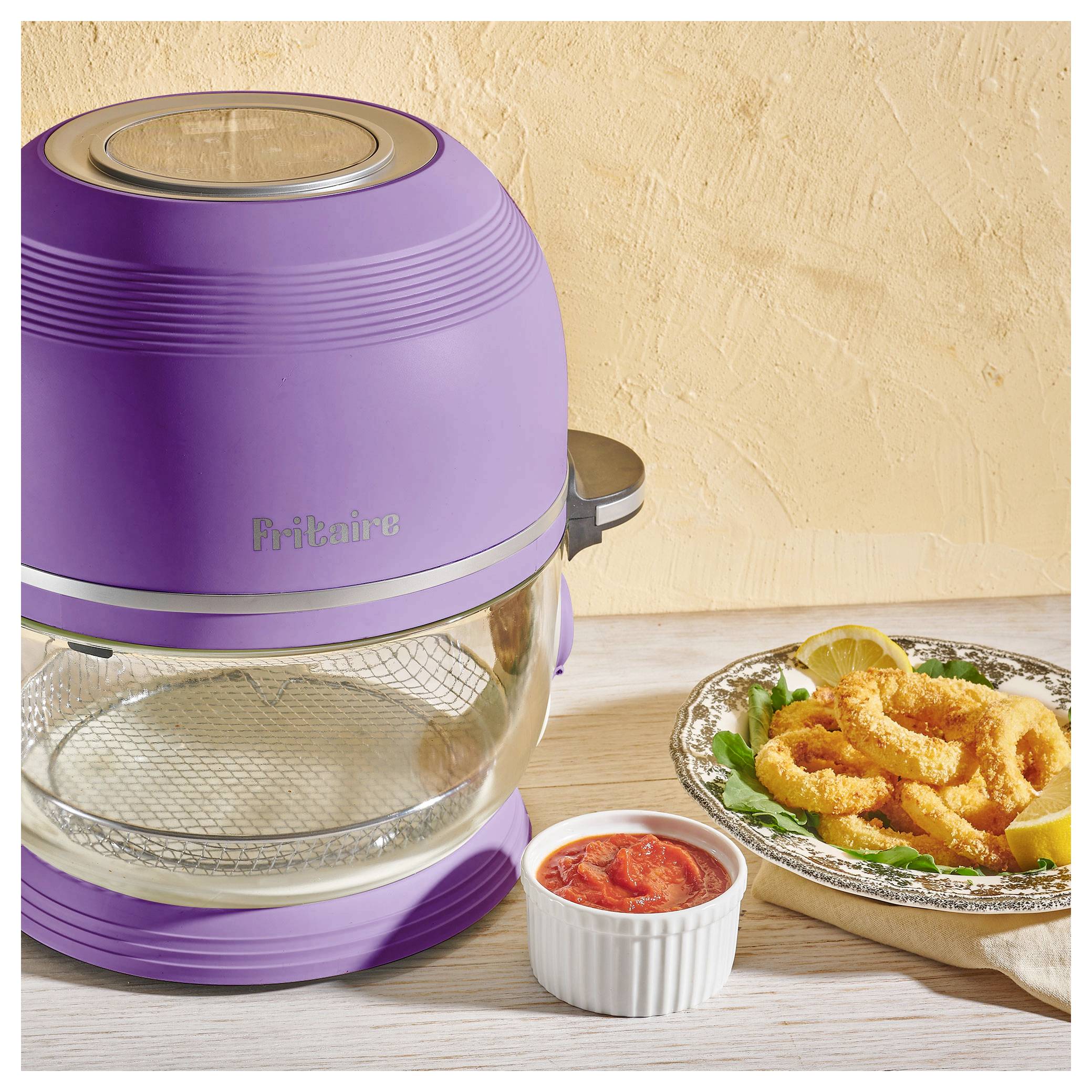 Ein lila Heißluftfritteuse steht auf einer Küchenarbeitsplatte neben einem Teller mit frittiertem Calamari, garniert mit Zitrone und Petersilie, und einer Ramekin mit Sauce.
