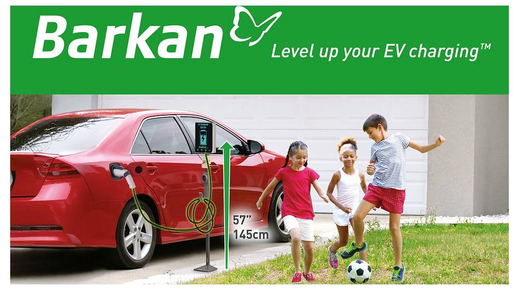 Ein rotes Elektrofahrzeug lädt in einer Einfahrt mit einer Barkan-Ladestation, während drei Kinder in der Nähe Fußball spielen.