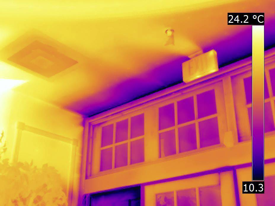 Thermisches Bild einer Zimmerdecke mit Temperaturunterschieden. Wärmere Bereiche in Gelb und kühlere Bereiche in Violett. Notausgangsschild sichtbar.