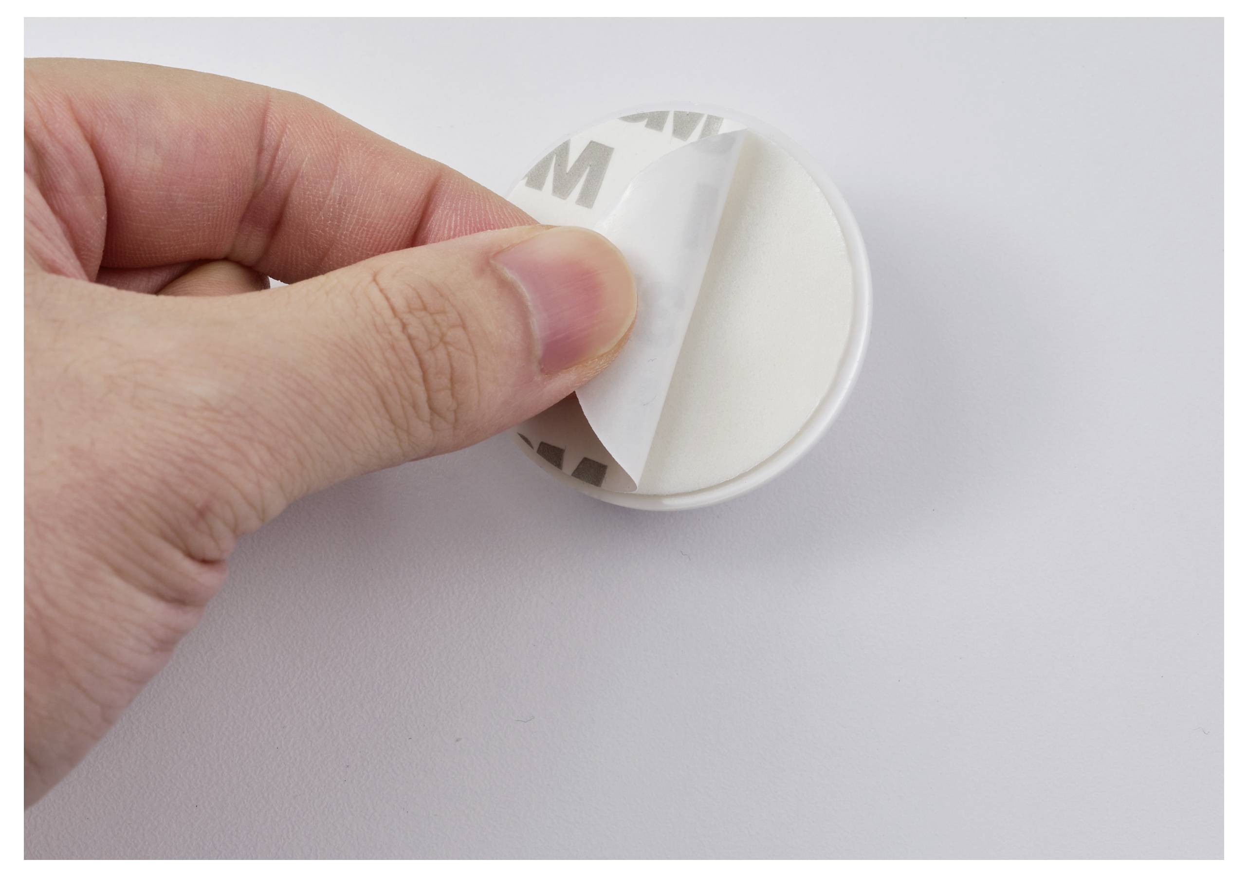 Eine Hand zieht die Schutzfolie von einem runden Haken oder Halterung ab und bereitet ihn zur Befestigung an einer Oberfläche vor.