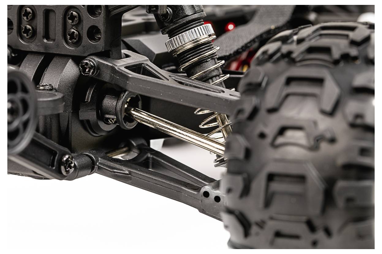 Nahaufnahme des Federungssystems eines Spielzeugautos, die filigrane Federn, einen Stoßdämpfer und einen großen strukturierten Reifen zeigt und mechanische Details hervorhebt.