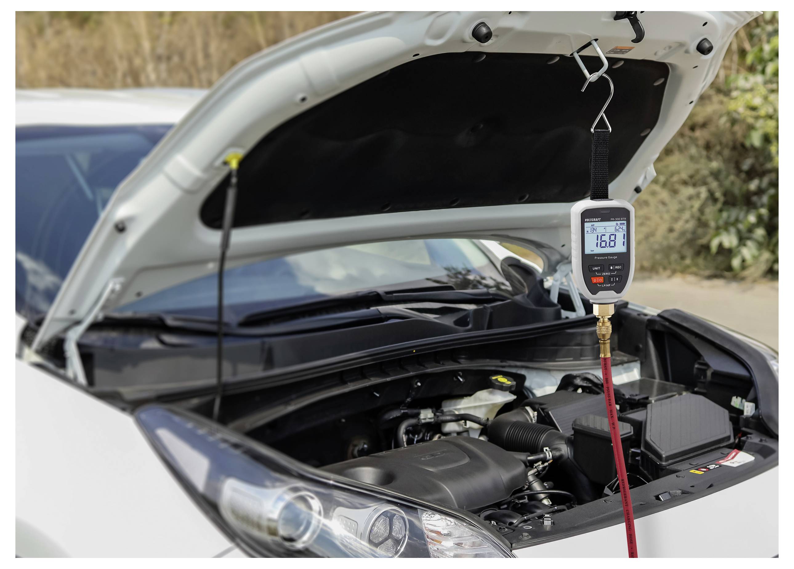 Ein Auto mit offener Motorhaube zeigt ein Klimaanlagen-Manometer, das „16,8
