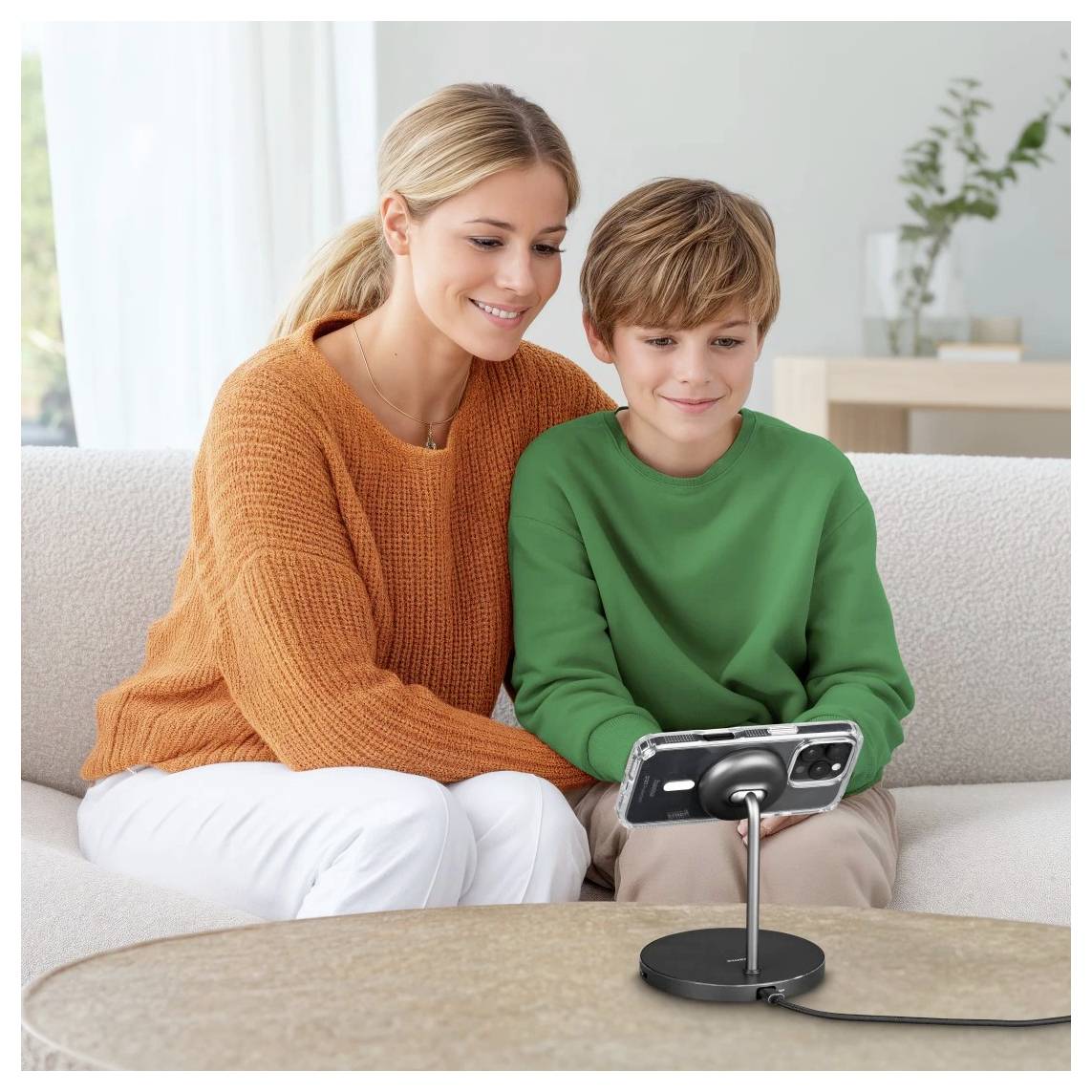 Eine Frau und ein Junge sitzen auf einem Sofa und lächeln auf ein Smartphone, das auf einem Ständer montiert ist, möglicherweise während eines Videoanrufs oder einer Aufnahme.