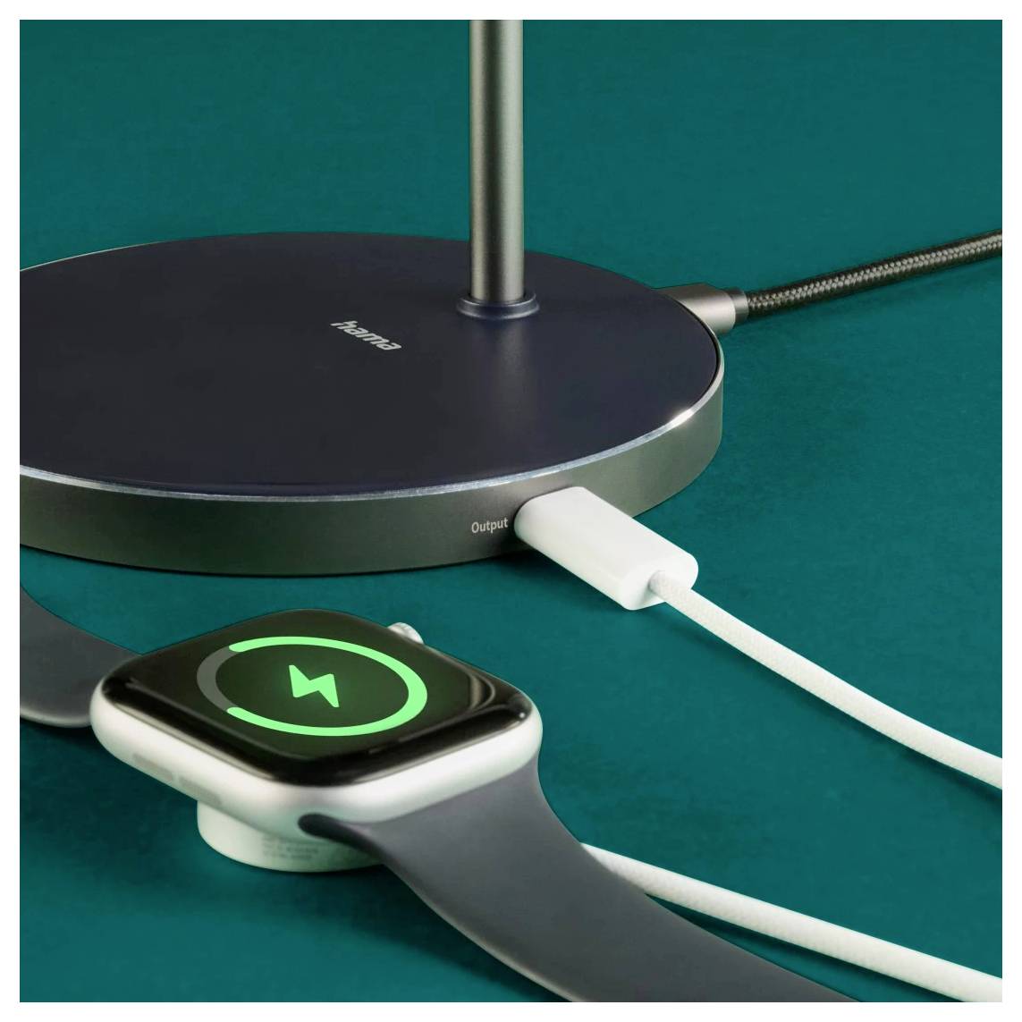 Eine Smartwatch mit einem grünen Ladeicon liegt auf einem drahtlosen Ladegerät, das mit einem Kabel verbunden ist und auf einer türkisfarbenen Oberfläche steht.