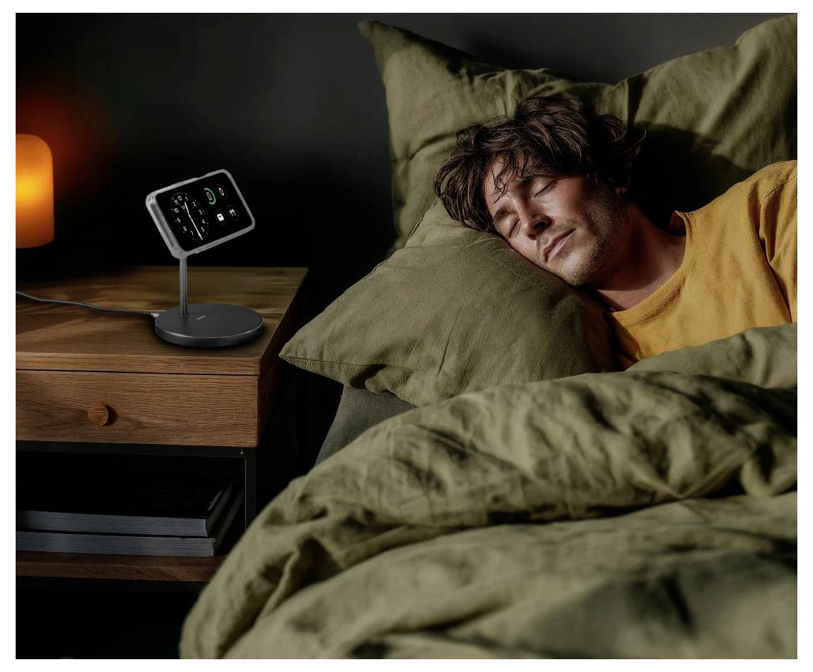 Eine Person schläft friedlich im Bett, während auf dem Nachttisch ein intelligentes Gerät mit Zeitanzeige und Warnungen einen gemütlichen, entspannten Ambiente schafft.