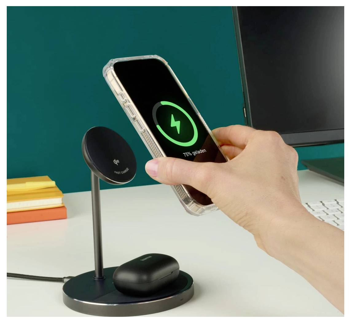 Eine Hand legt ein Smartphone auf einen drahtlosen Ladegerät auf einem Schreibtisch. Das Telefon zeigt '75% Akkuladung.' Eine Ladehülle liegt auf dem Ständer.