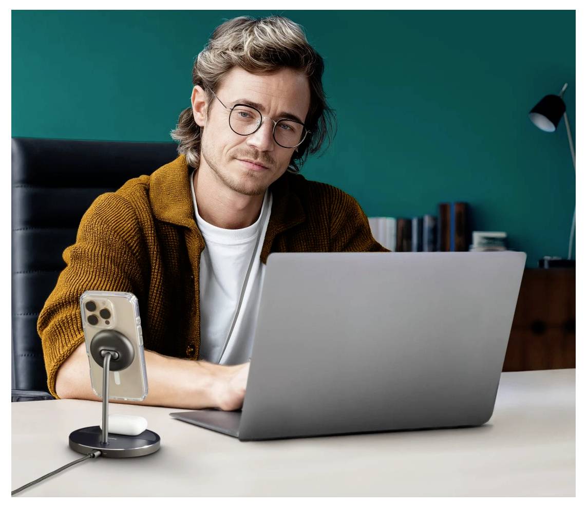 Eine Person mit Brille und einem braunen Cardigan, die an einem Schreibtisch an einem Laptop arbeitet, mit einem Smartphone, das auf einem Ständer in der Nähe montiert ist.