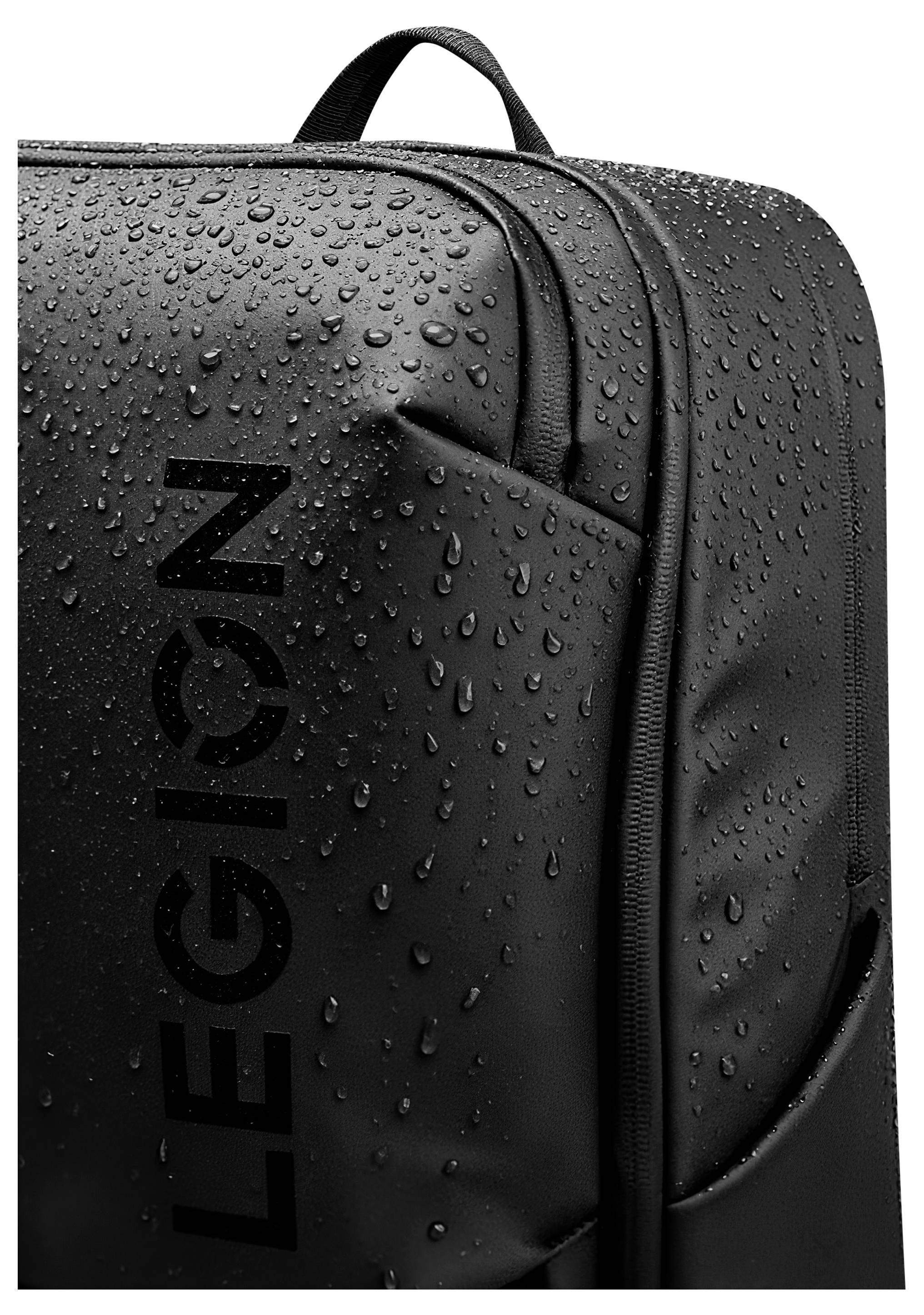 Eine Nahaufnahme eines schwarzen Rucksacks mit Wassertropfen auf seiner Oberfläche, die das wasserabweisende Material demonstrieren. Das Wort ‚LEGION' ist vertikal aufgedruckt.