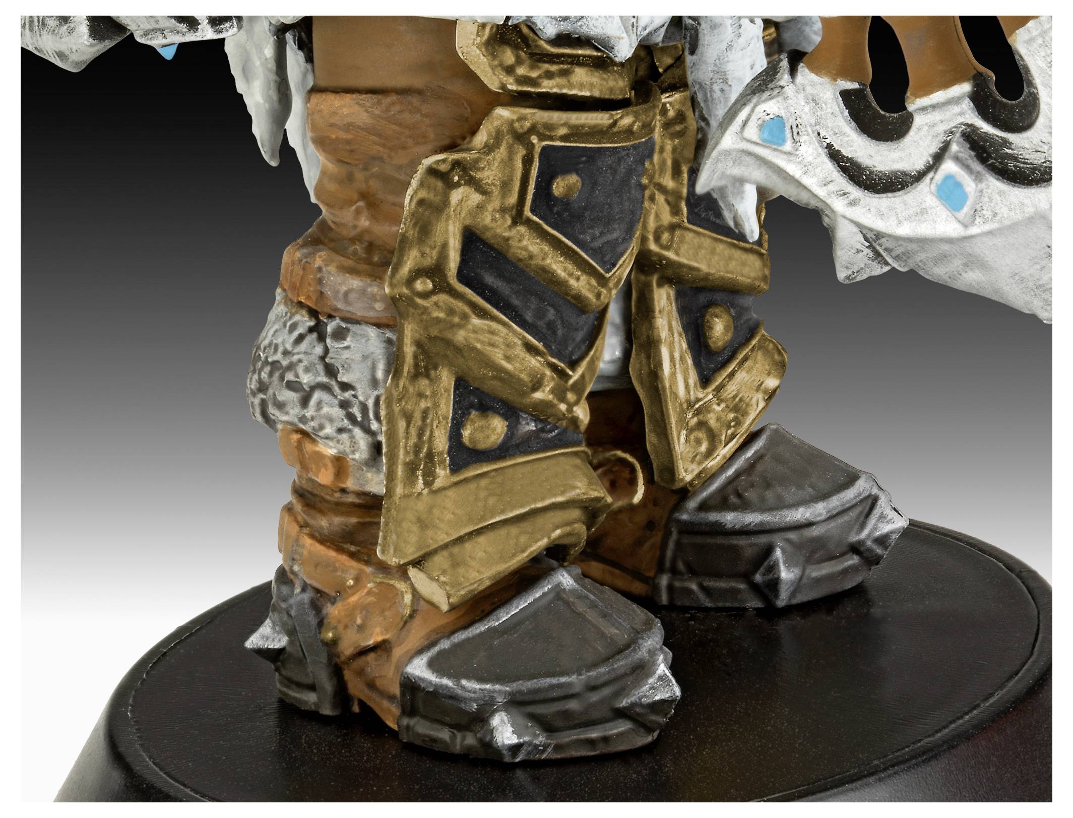 Eine detaillierte Nahaufnahme der gepanzerten Stiefel einer Statue, mit komplexen Gold- und Silberdesigns und scharfen, kantigen Mustern auf einer runden Basis.