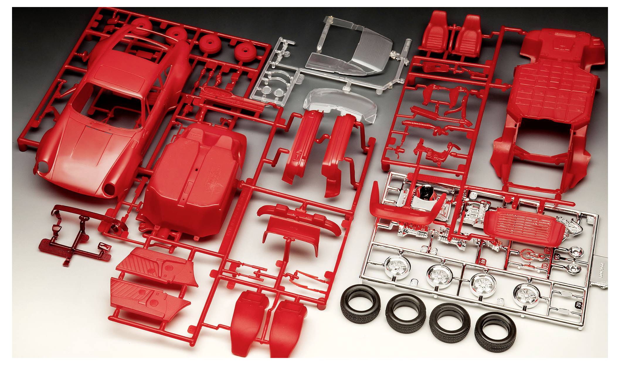 Ein rotes Modell-Auto-Bausatz mit verschiedenen Teilen wie Fahrzeugkarosserie, Rädern und Innenausstattungskomponenten, die auf Anspritzrahmen angeordnet sind und zur Montage bereitstehen.