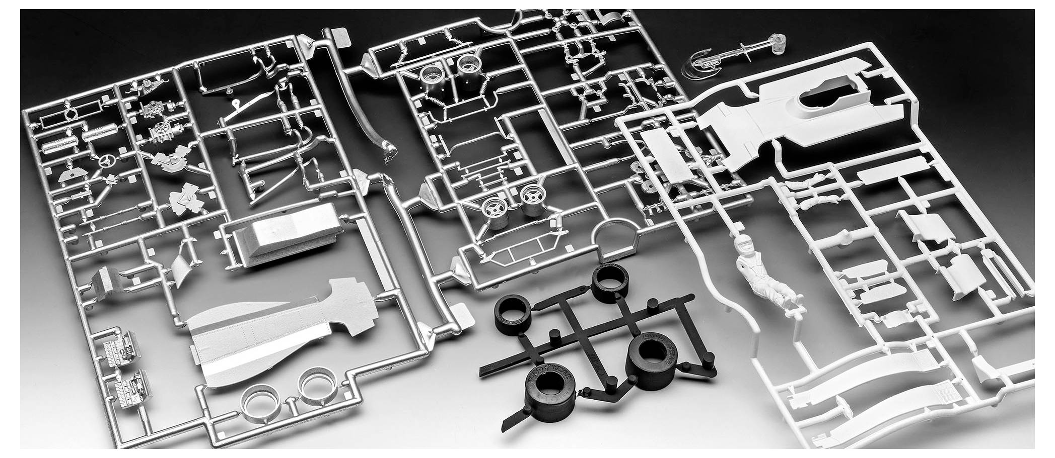 Plastikmodellbausatz-Teile, die auf einem Tisch in ordentlicher Weise ausgelegt sind und verschiedene Teile zur Montage zeigen, einschließlich Rädern und Karosseriekomponenten.