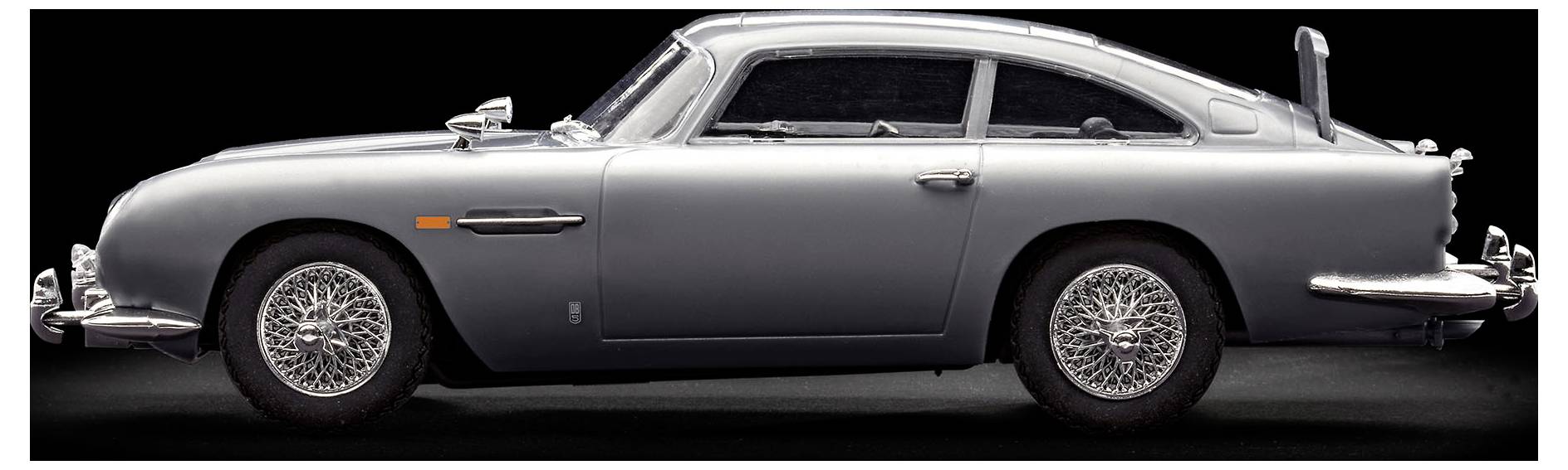 Ein silberner Oldtimer-Sportwagen wird im Profil vor einem dunklen Hintergrund gezeigt, wobei sein elegantes Design und seine Chromdrahtspeichenräder hervorgehoben werden.