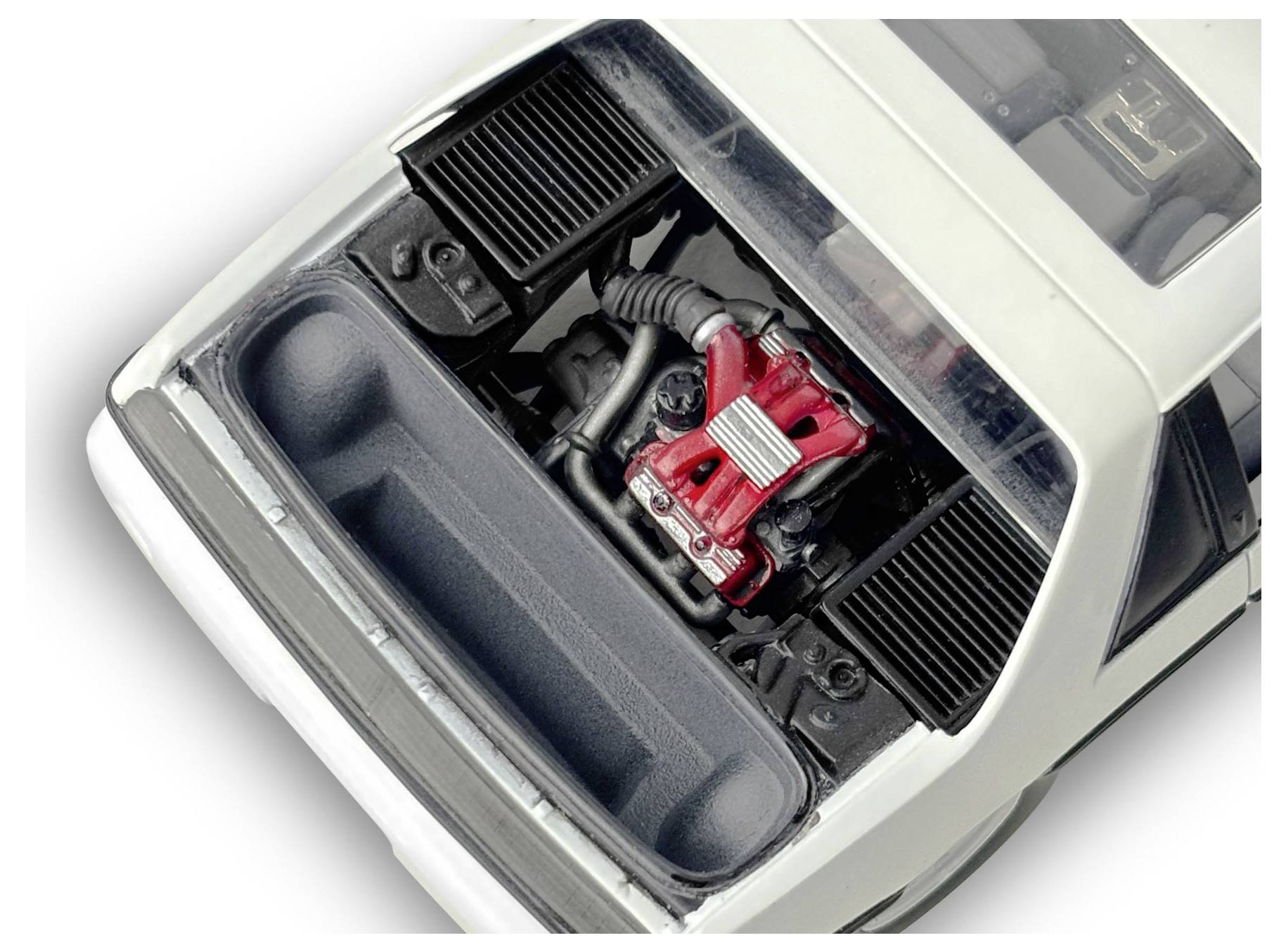Ein Modellauto mit geöffneter Motorhaube, die detaillierte Motorkomponenten in Rot und Silber innerhalb eines weißen Autos offenbart.