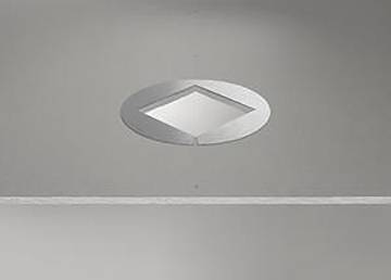 Eine runde metallische Schaltfläche mit einem diamantförmigen Design in der Mitte vor einem matter grauen Untergrund scheint ein Element einer Fahrstuhlsteueranlage zu sein.