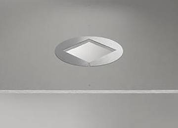 Eine verspiegelte, rautenförmige Fliese, die in eine graue Wand eingelassen ist und Licht reflektiert.