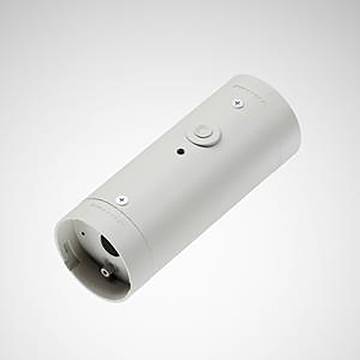 Eine zylindrische, graumetallische Komponente mit einem kleinen Knopf und zwei Öffnungen an den Enden, möglicherweise Teil einer industriellen oder mechanischen Vorrichtung.