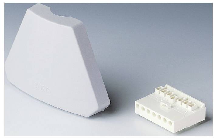 Ein grau, abgerundetes dreieckiges Kunststoffteil neben einem weißen, rechteckigen Elektrostecker mit mehreren Schlitzen auf einer glatten Oberfläche.