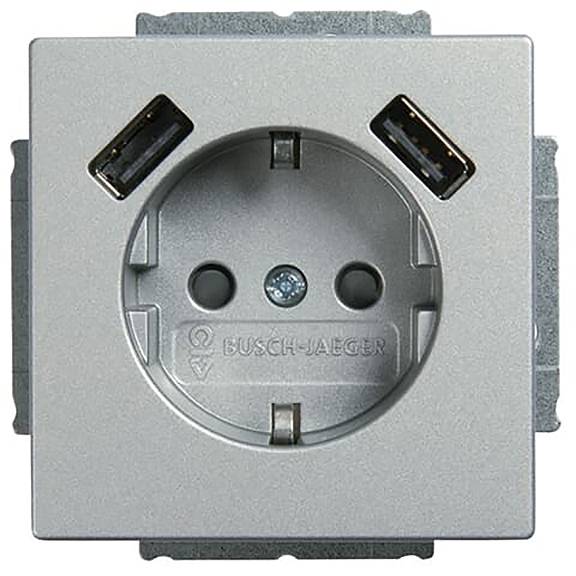 Eine silberfarbene elektrische Steckdose mit zwei integrierten USB-Anschlüssen an den oberen Ecken, gekennzeichnet mit 'BUSCH-JAEGER' am unteren Ende der Steckdose.