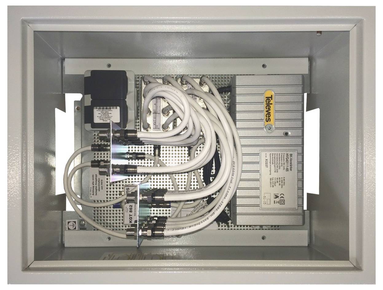 Eine Metallbox enthält ein Telekommunikationsgerät mit mehreren weißen Kabeln, die mit Anschlüssen auf der inneren Platte verbunden sind, die mit 