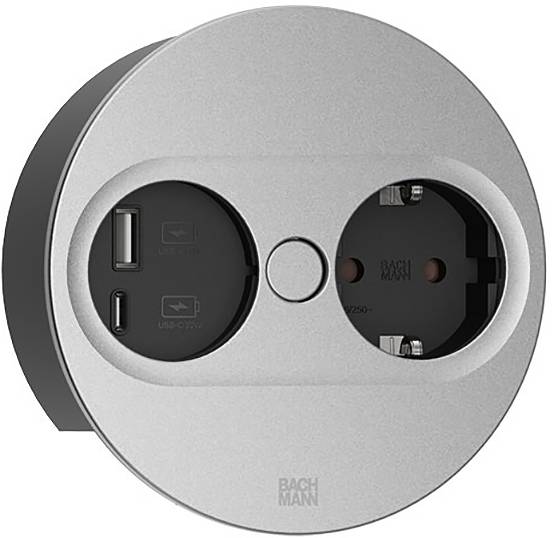 Kreisförmige Doppelsteckdose mit USB-Anschlüssen auf der linken Seite und europäischer Steckdose auf der rechten Seite. Silberne Oberplatte mit 'Bachmann'-Branding.