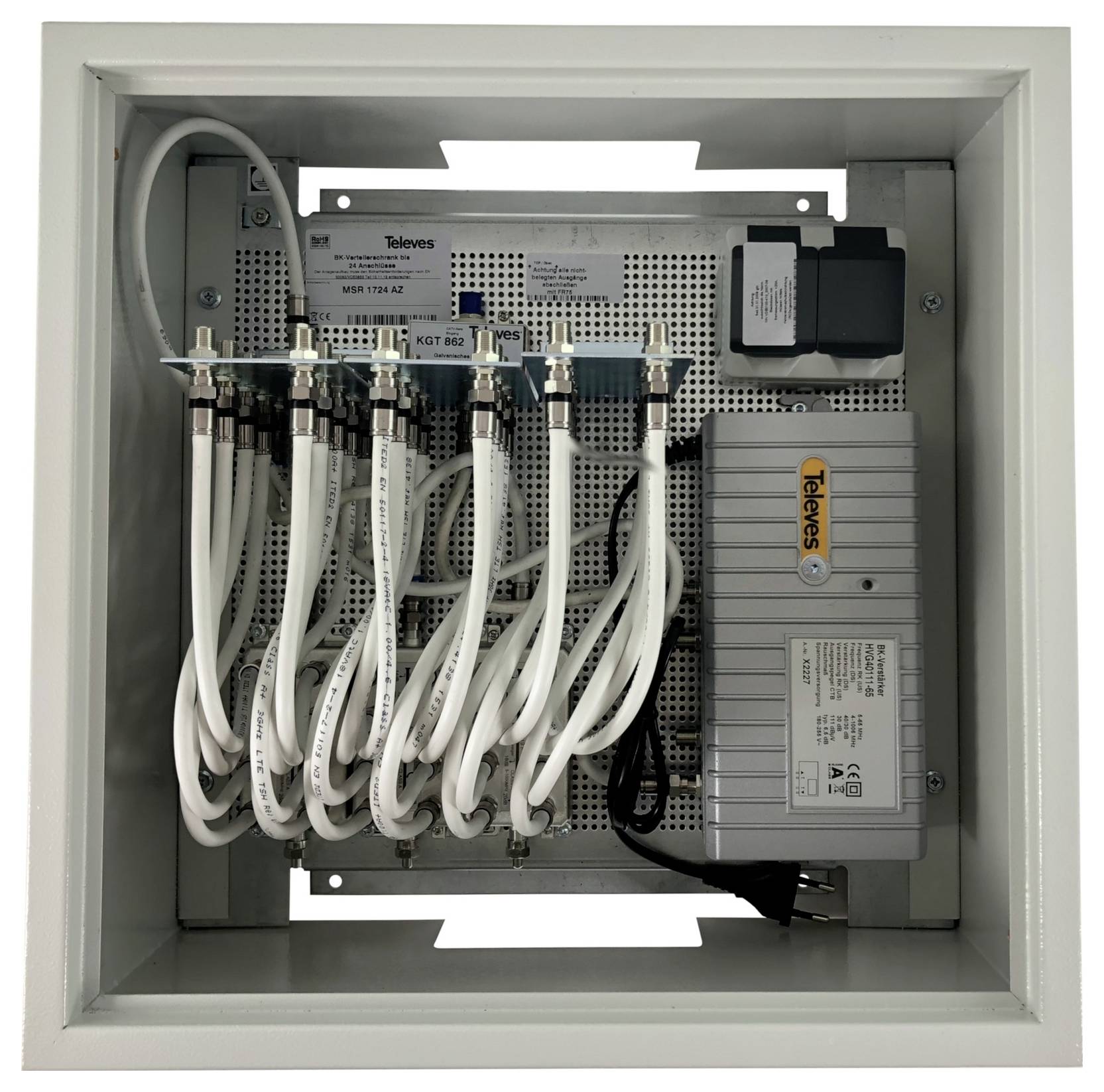 Ein weißes Gehäuse mit einem Netzwerk-Verteilerpanel mit mehreren Koaxialkabeln, die mit einer Zentraleinheit verbunden sind, die als Televes bezeichnet ist.