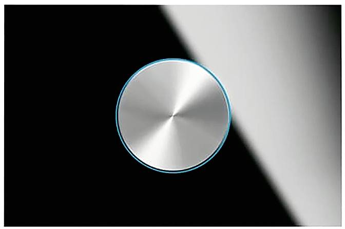 Ein kreisförmiger metallischer Knauf mit glatter gebürsteter Oberfläche, vor einem schwarz-grauen Farbverlaufshintergrund, der die Kante des Knaufs hervorhebt.