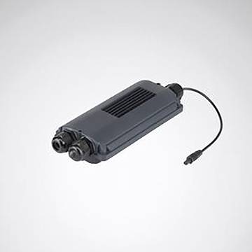 Ein rechteckiges, dunkel gefärbtes elektronisches Gerät mit zwei Anschlüssen an einem Ende und einem verbundenen Kabel am anderen Ende, vor einem hellen Hintergrund.