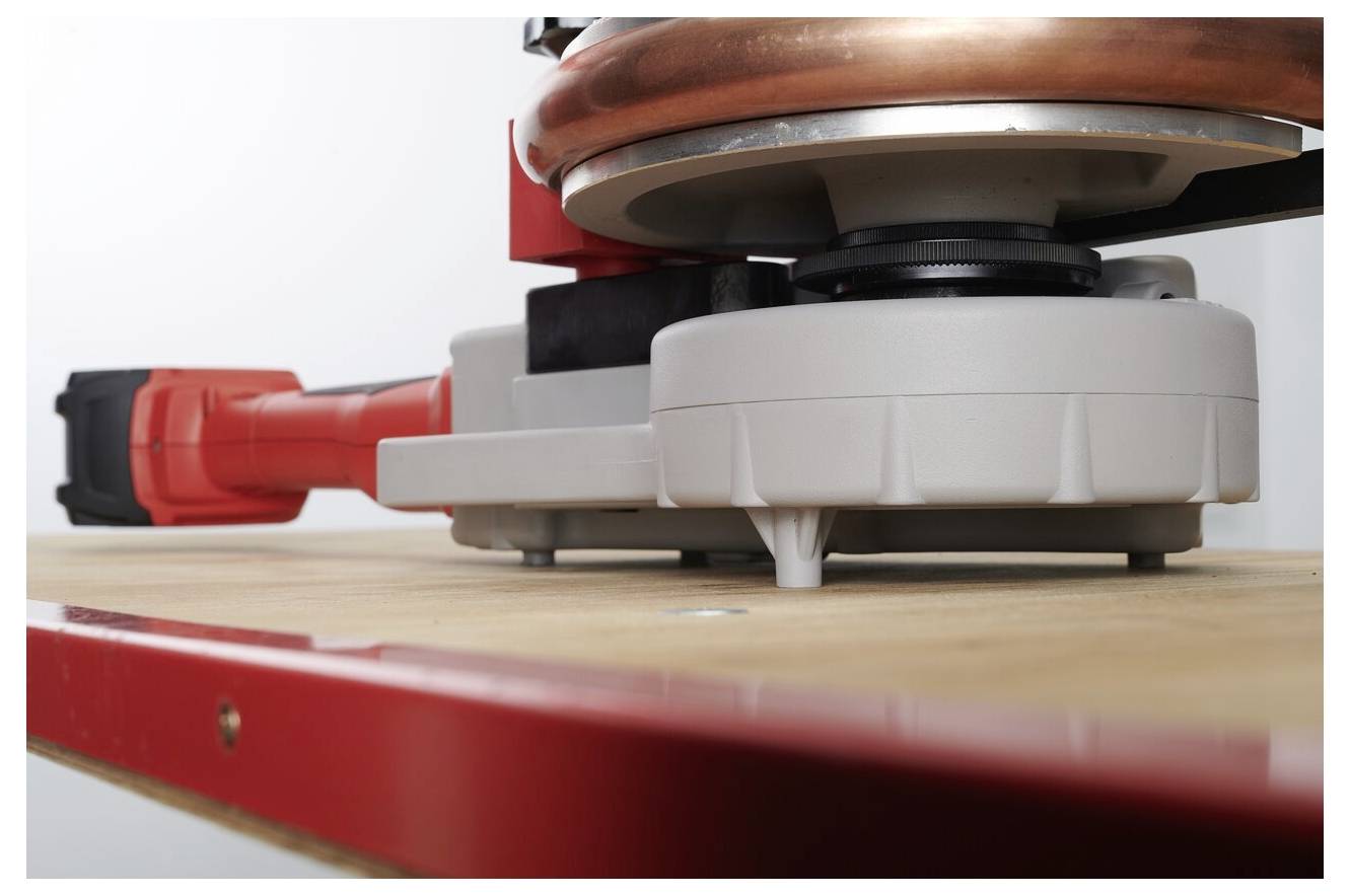 Ein Nahaufnahme eines Elektrowerkzeugs, das auf einer Holzoberfläche ruht und einen roten Griff sowie eine kreisförmige Kupferkomponente aufweist, die wahrscheinlich für industrielle Zwecke vorgesehen ist.