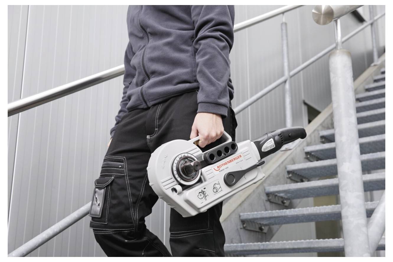 Person mit einer großen, weißen, tragbaren Maschine mit roter Beschriftung, die eine Metalltreppe hinuntergeht und dunkle Kleidung trägt.