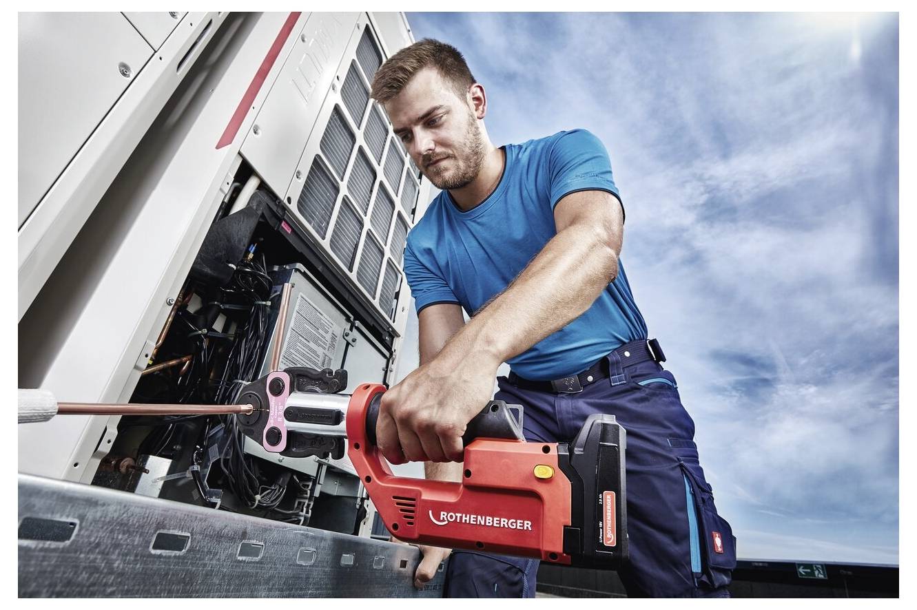 Ein Techniker verwendet ein rotes Werkzeug mit der Aufschrift ‚ROTHENBERGER', um elektrische Geräte im Freien zu warten, und trägt dabei eine blaue Uniform unter einem bewölkten Himmel.