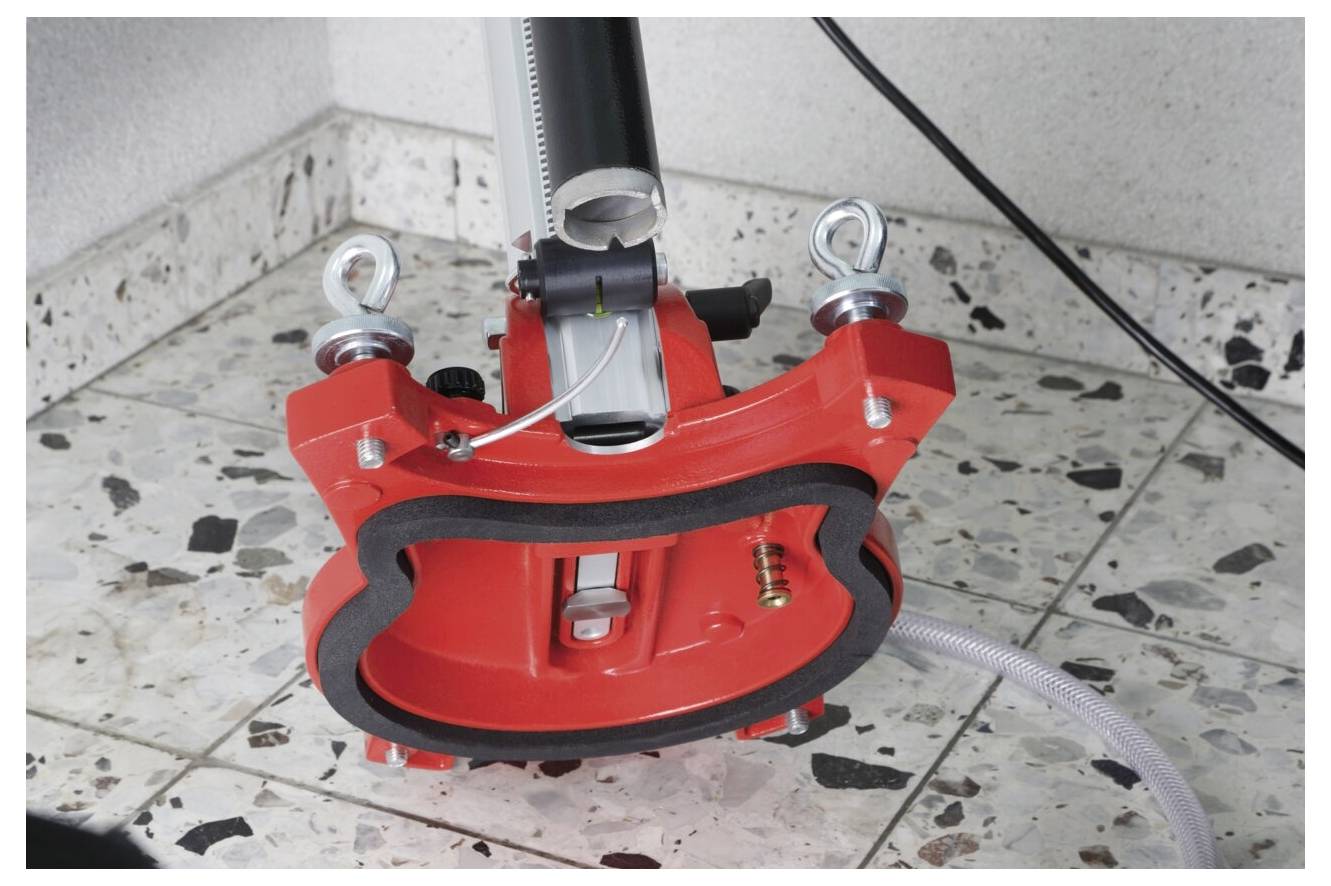 Eine rote, industrielle Saugverankerung, die an einem Terrazzoboden befestigt ist, mit Kabeln und einem Schlauch, und dazu dient, Ausrüstung oder Strukturen zu sichern.