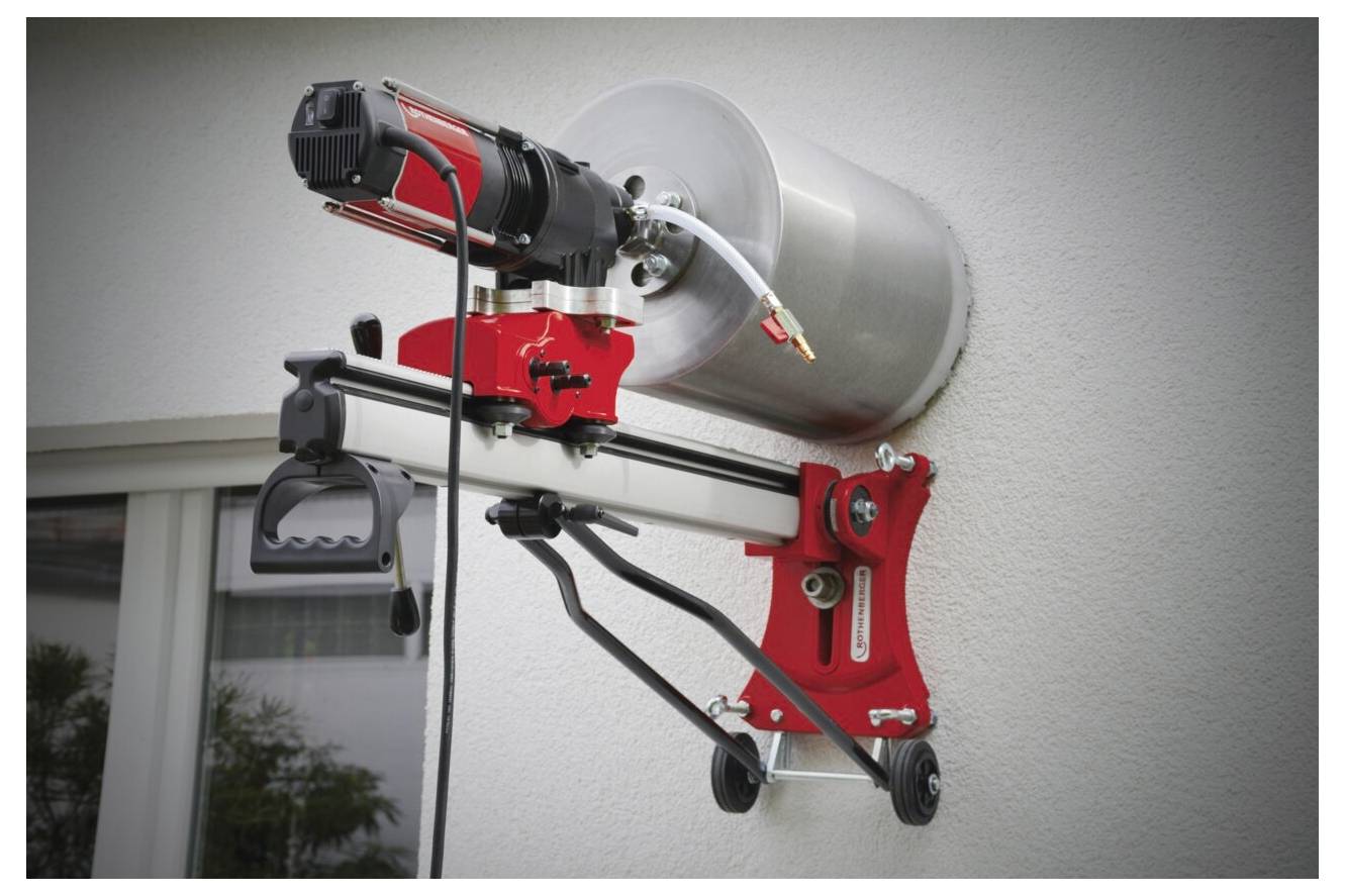 Eine rot-schwarze, an der Wand montierte Maschine mit Motor ist in der Nähe eines Fensters positioniert und für das Bohren oder Kernbohren in eine Betonoberfläche ausgelegt.